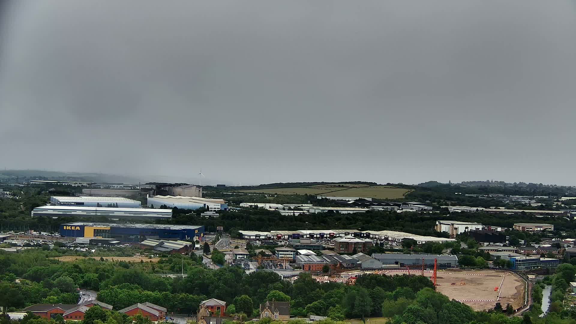 An aerial view shows an industrial area with a large blue IKEA building, under an overcast sky.