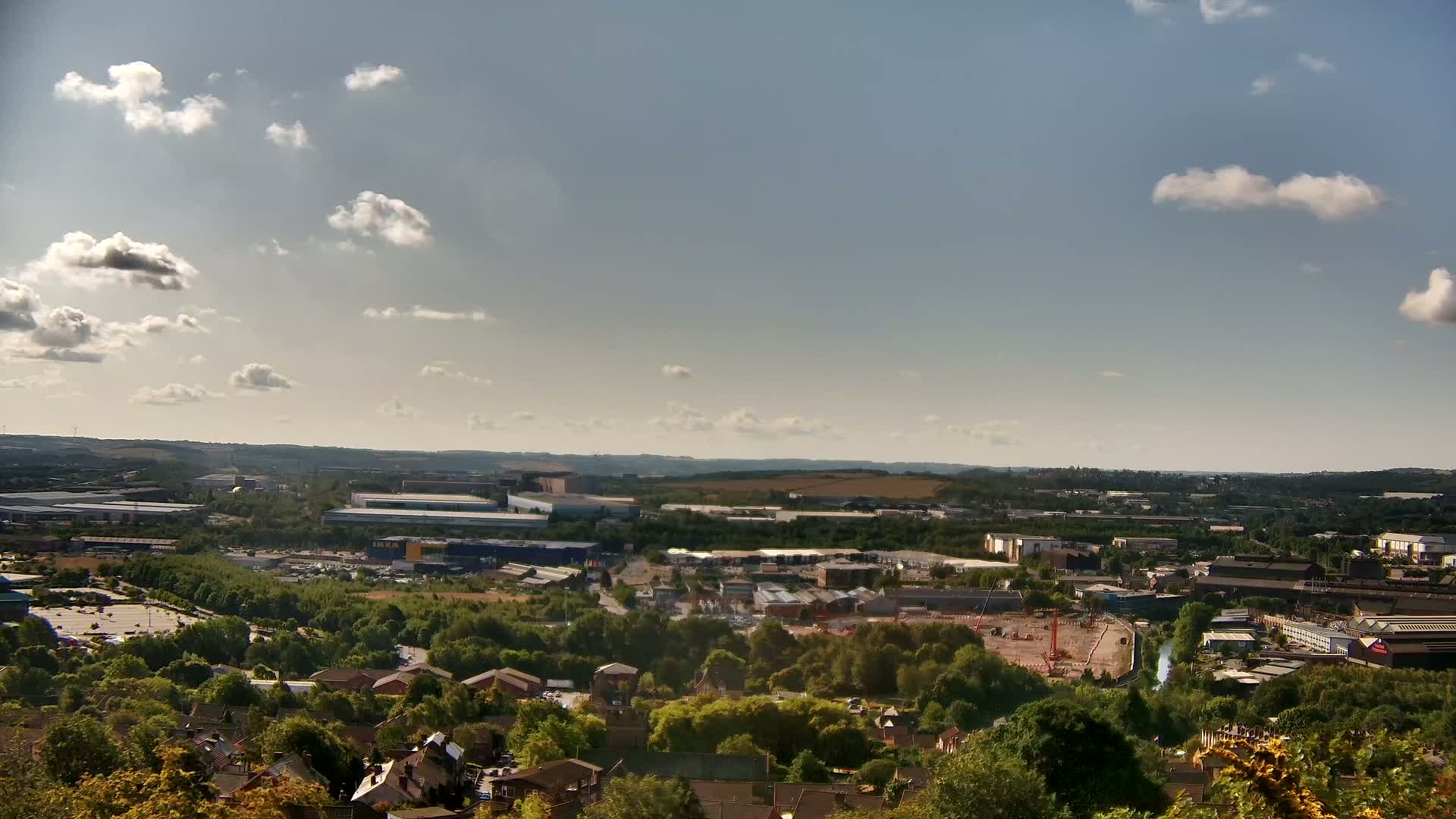 A sprawling industrial area and residential neighborhood are visible from a high vantage point on a partly sunny day with scattered clouds.