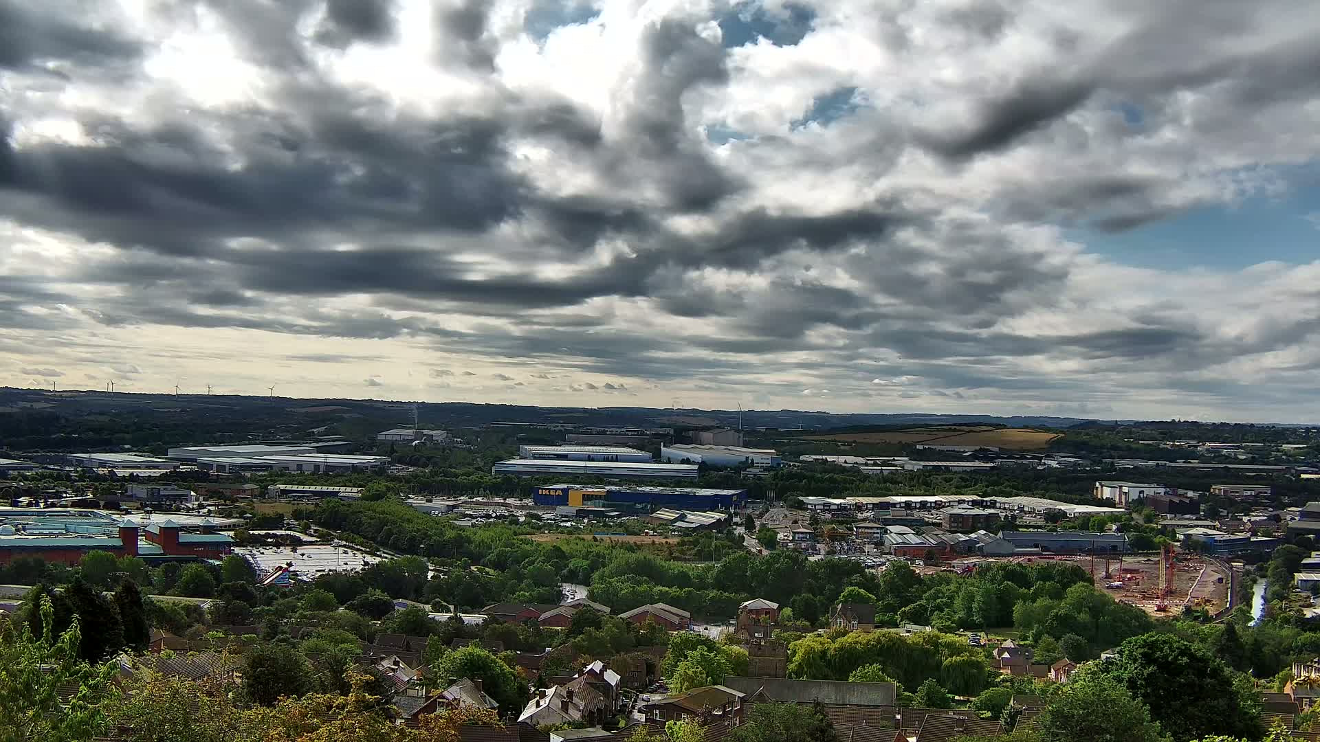 A panoramic view of a suburban area with industrial buildings and a large retail store under a partly cloudy sky.