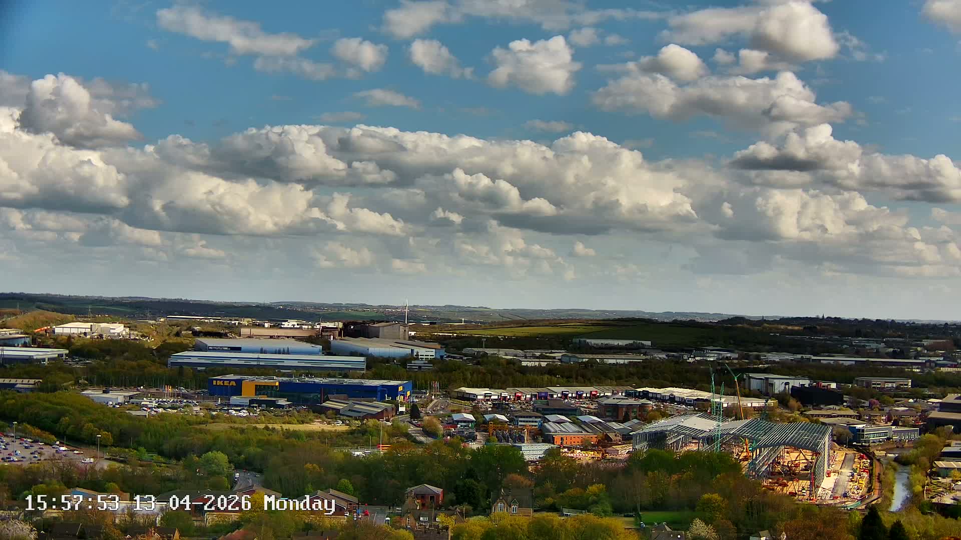 A wide view captures a vast urban and industrial landscape at sunrise, with the sky displaying a mix of blue, grey, and golden-orange clouds, as factories emit steam into the clear morning air.