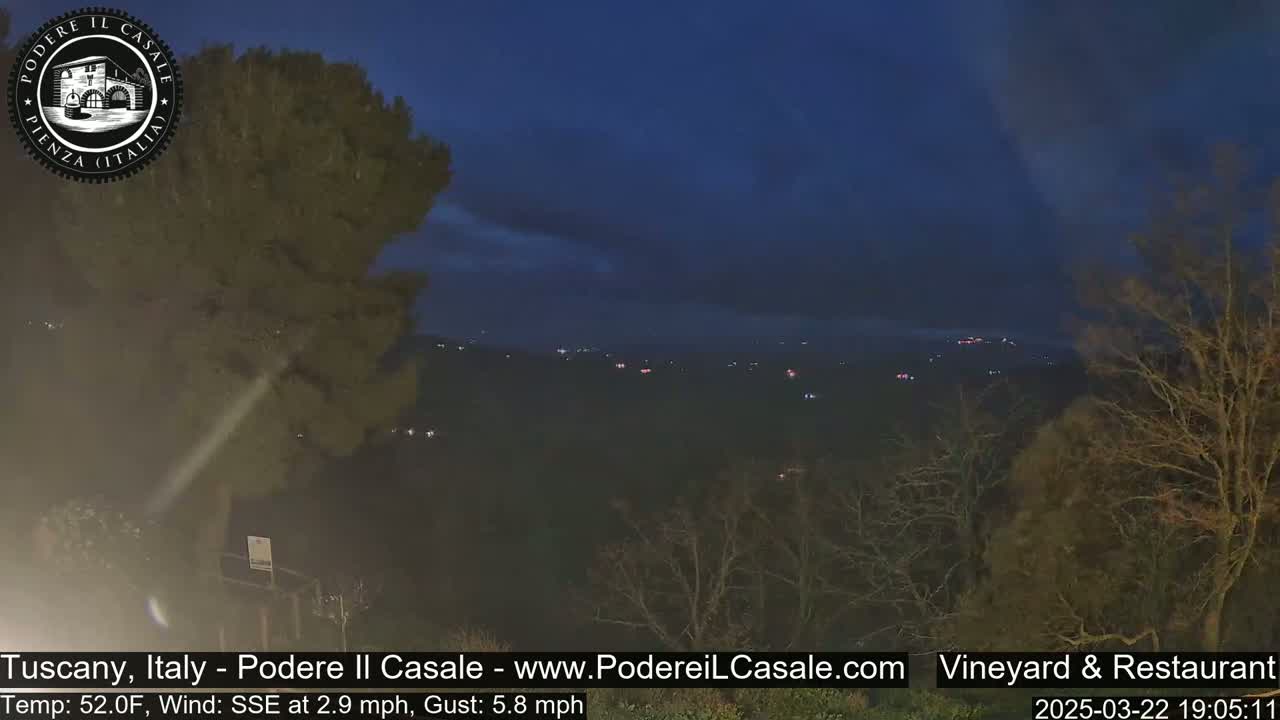 A nighttime view of a dark, hilly landscape with scattered lights, under a mostly clear, dark blue sky.