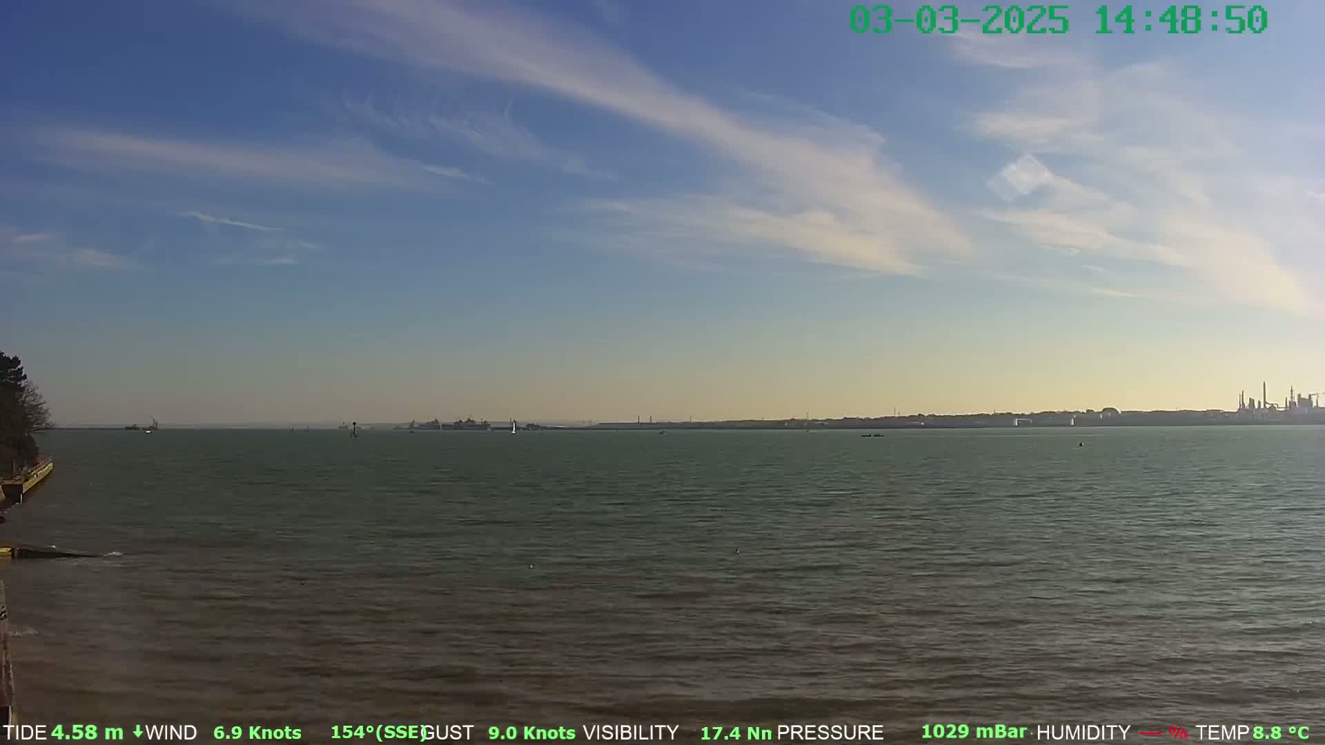 A calm body of water stretches to a distant shoreline under a mostly clear sky with wispy clouds.