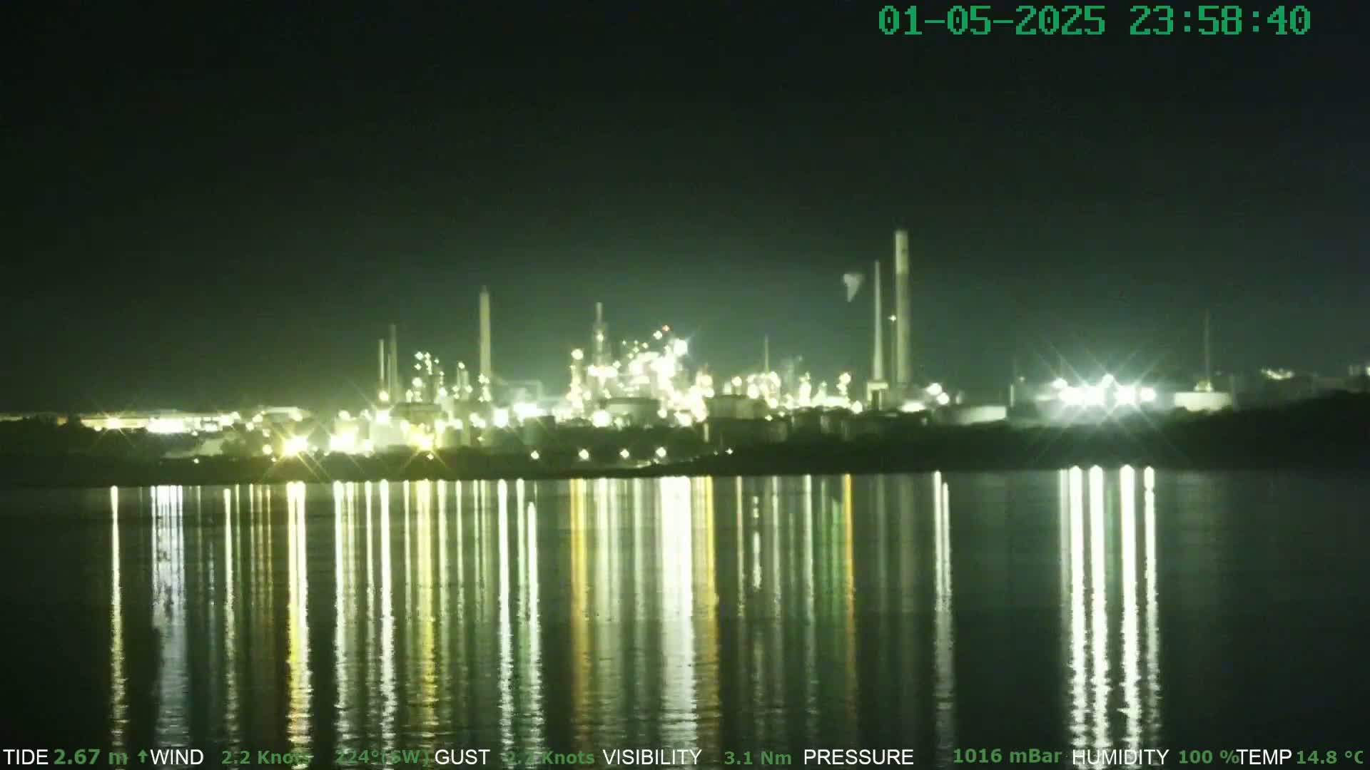 At night, a brightly lit industrial complex is reflected in a calm body of water.
