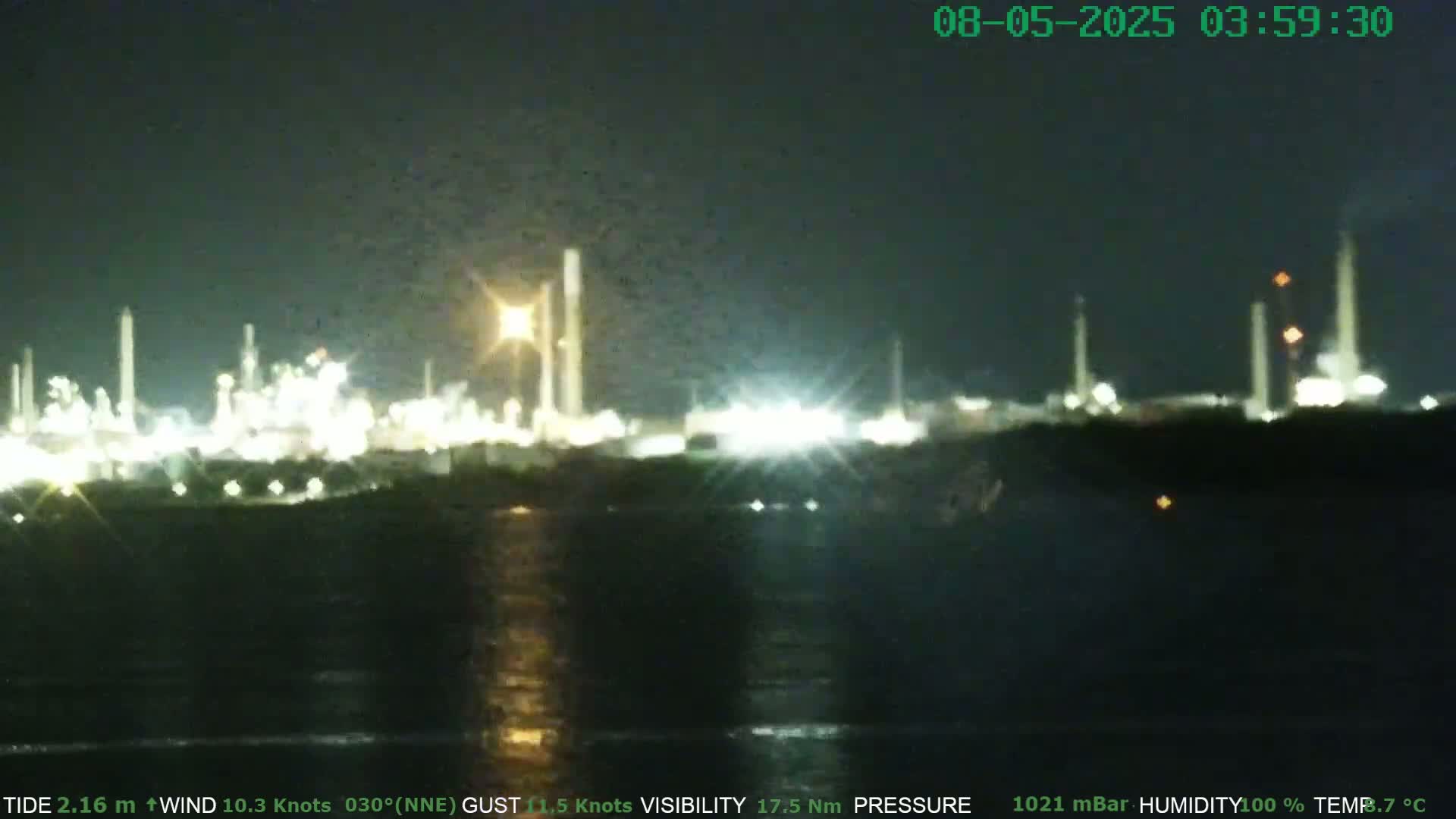 A brightly lit industrial plant is seen across a dark body of water at night.
