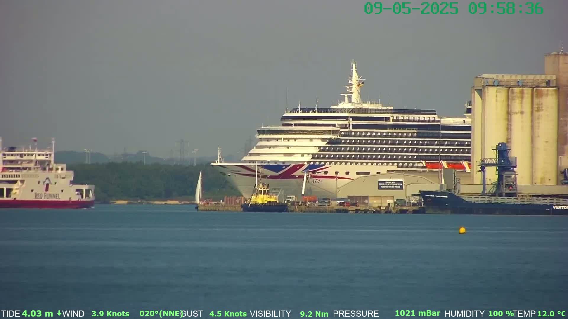 A large cruise ship is docked near a ferry and industrial buildings on a hazy day.