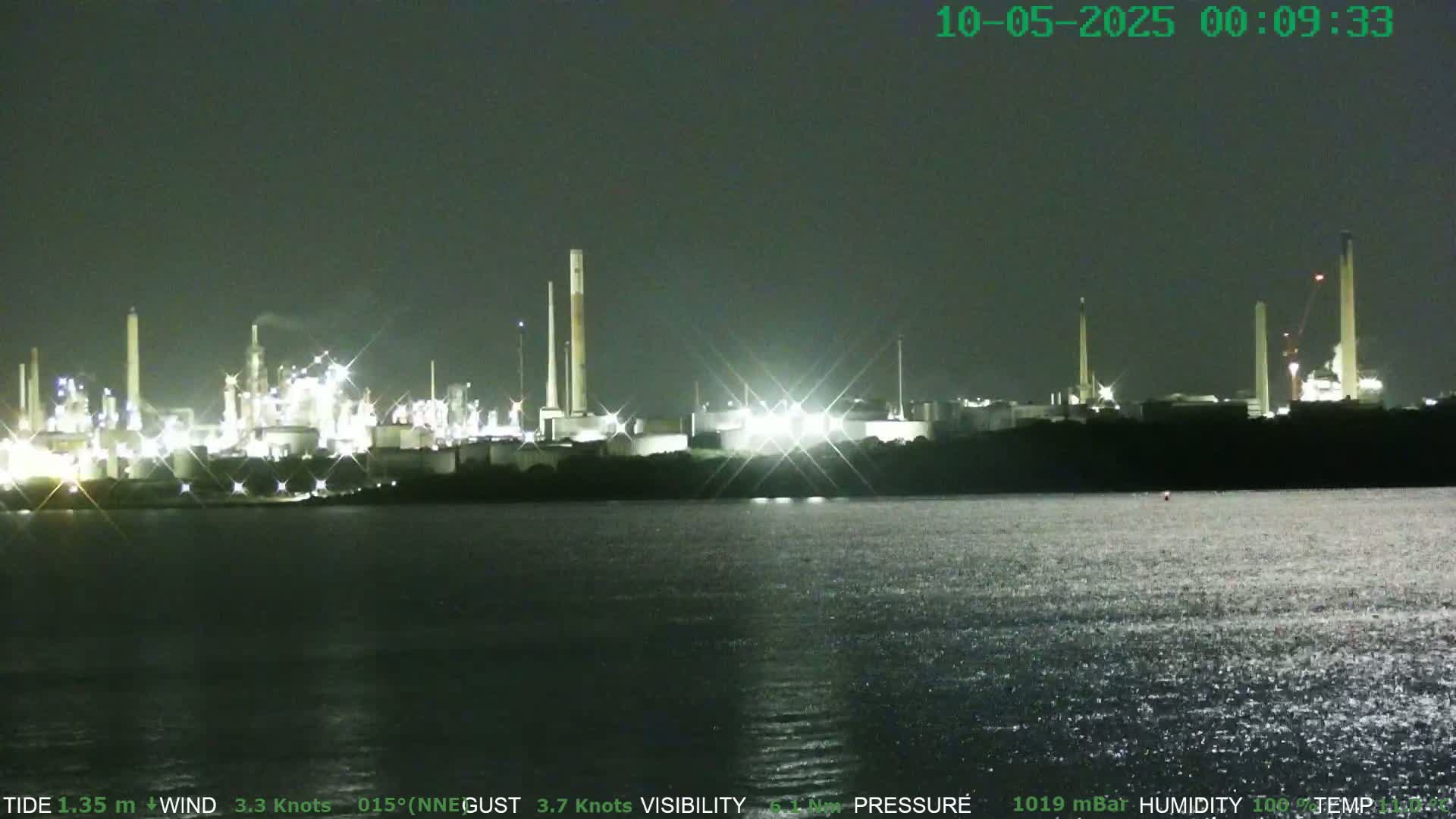 A brightly lit industrial complex is visible across a dark body of water at night.