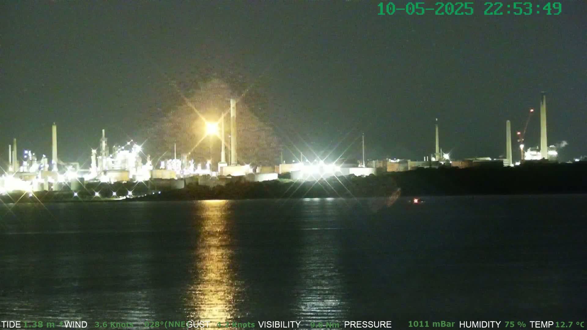 A brightly lit industrial plant is situated on the far shore of a dark body of water at night.