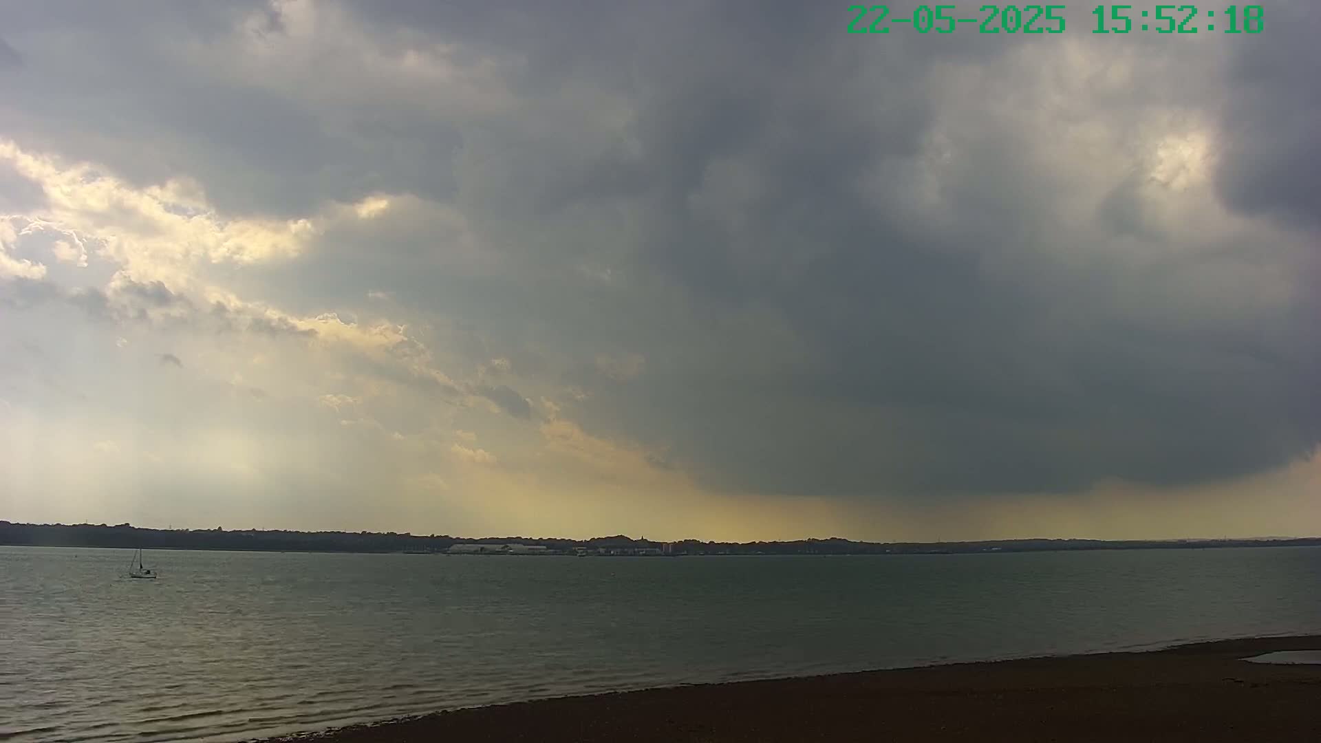 A sailboat is visible on a calm body of water under a partly cloudy sky, with a large, dark cloud mass dominating the horizon.