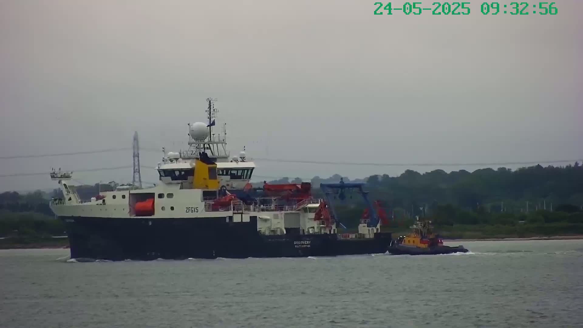 A large research vessel is being assisted by a smaller tugboat on a calm, overcast day.