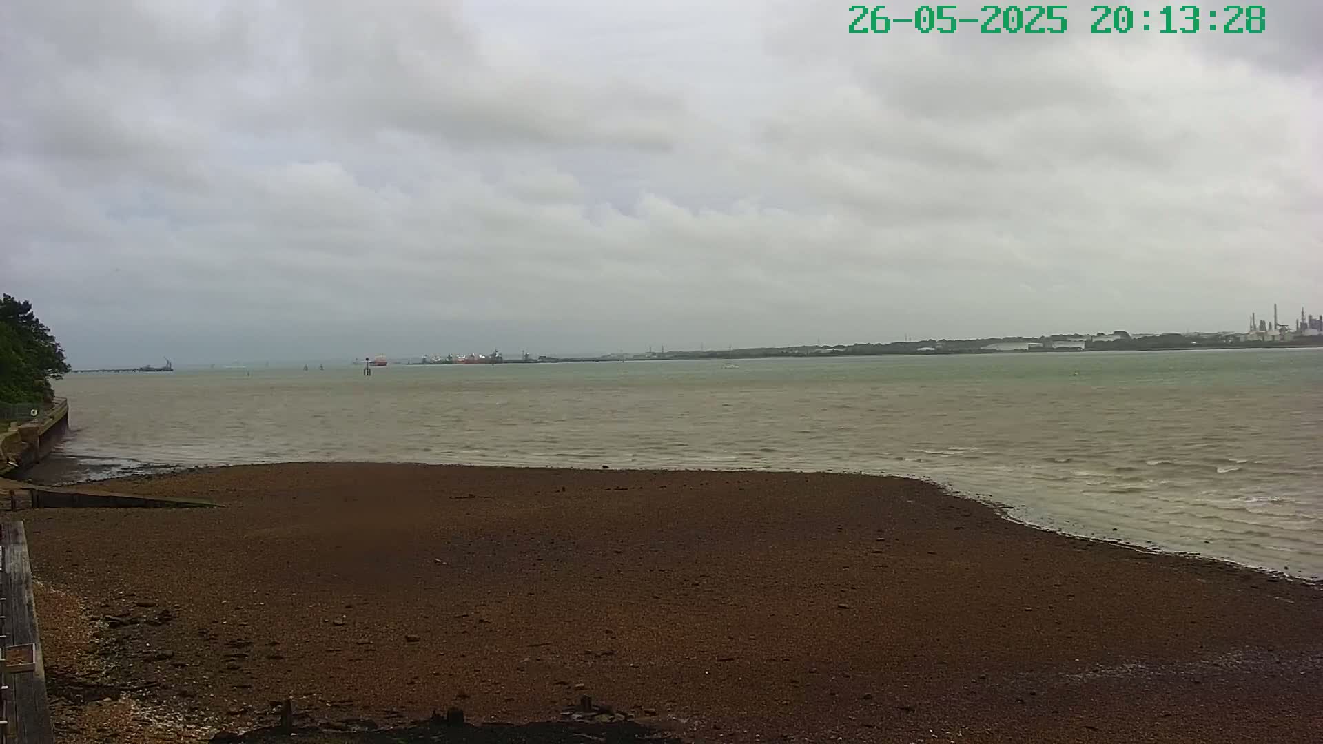 A dark brown, pebbly beach slopes down to a choppy, grayish-green body of water under an overcast sky.