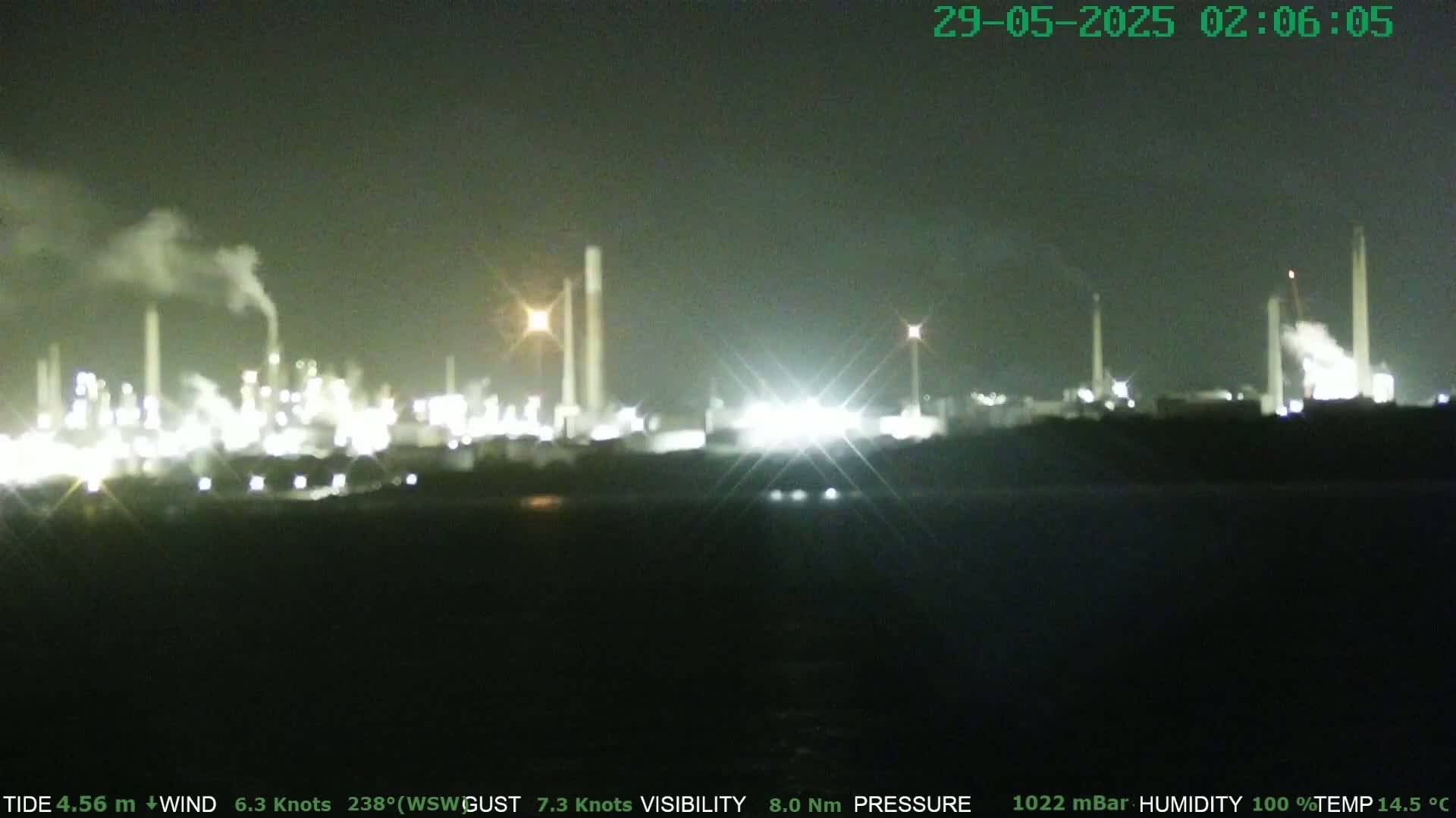 A brightly lit industrial plant at night, emitting smoke, is visible under a dark sky.