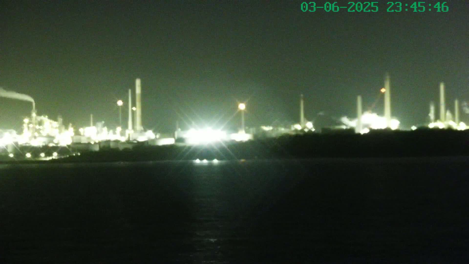 A brightly lit industrial plant is visible across a dark body of water at night.
