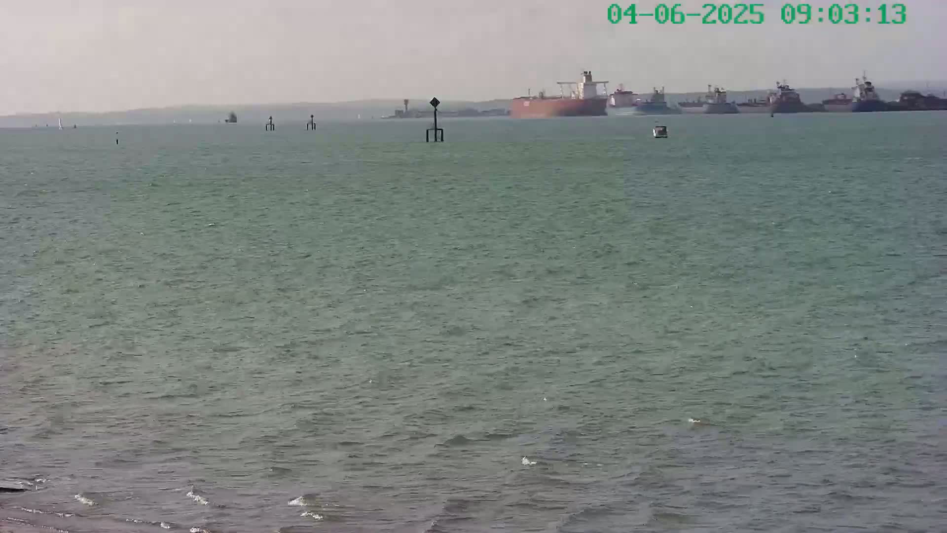 A calm body of water shows several ships in the distance under a hazy sky.