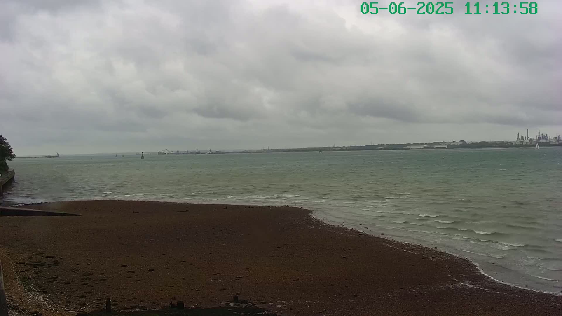 A dark-colored, pebbly beach meets a choppy, greenish-grey sea under a cloudy sky.