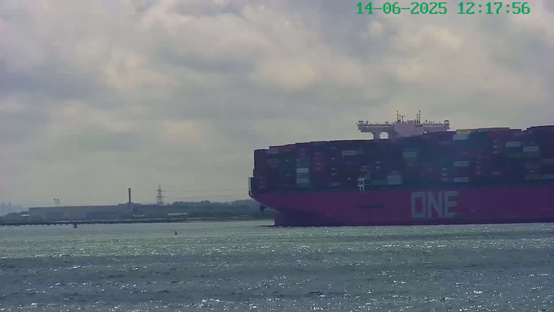 A large container ship is on the water under a cloudy sky.
