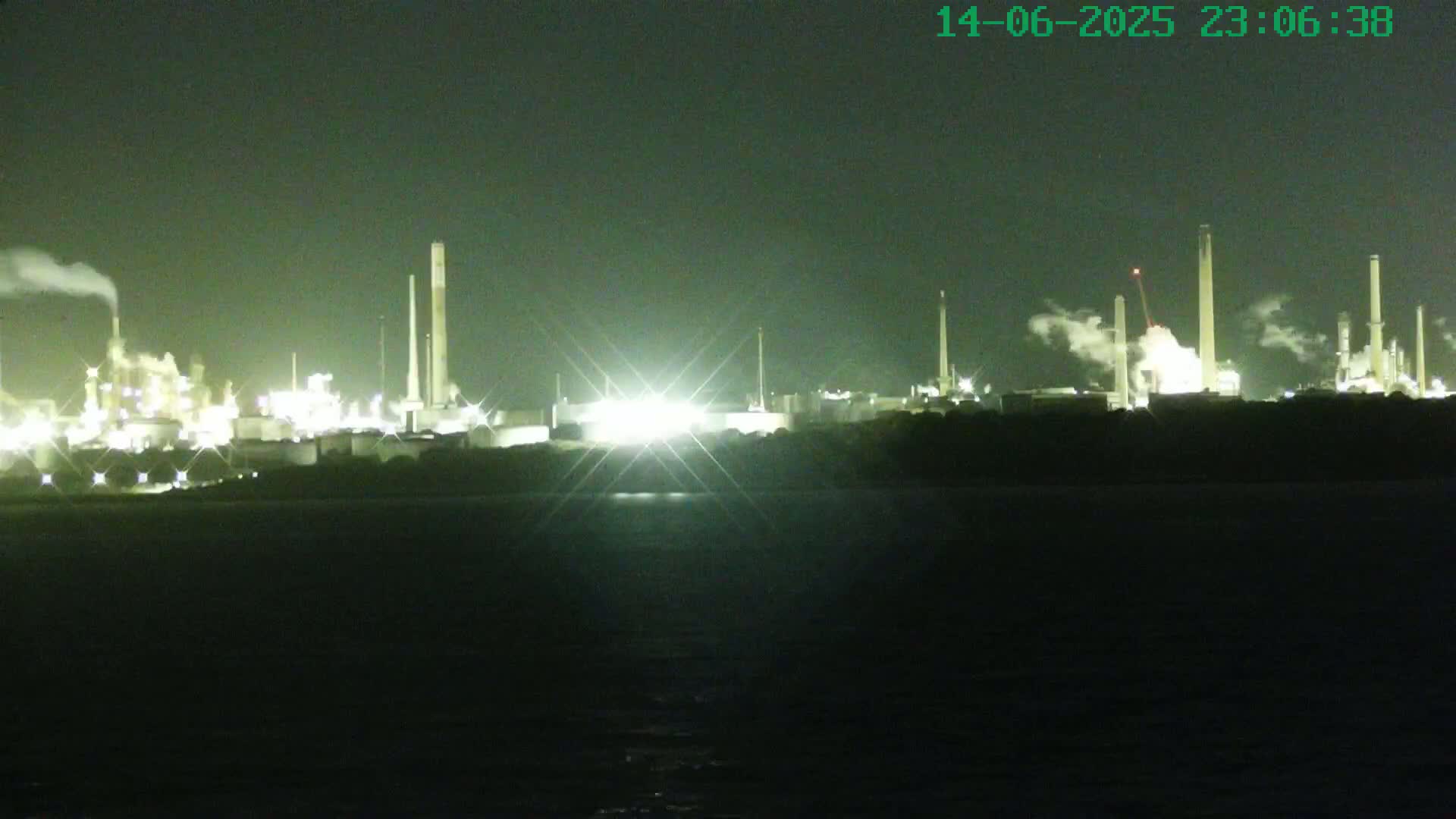 A large cruise ship is docked near an industrial area on a partly cloudy day.