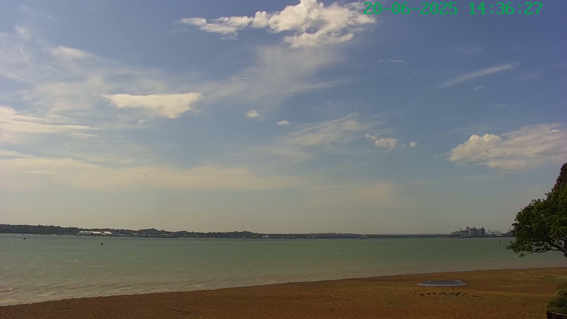 A partly cloudy sky overlooks a calm body of water with a sandy beach in the foreground and a distant shoreline.