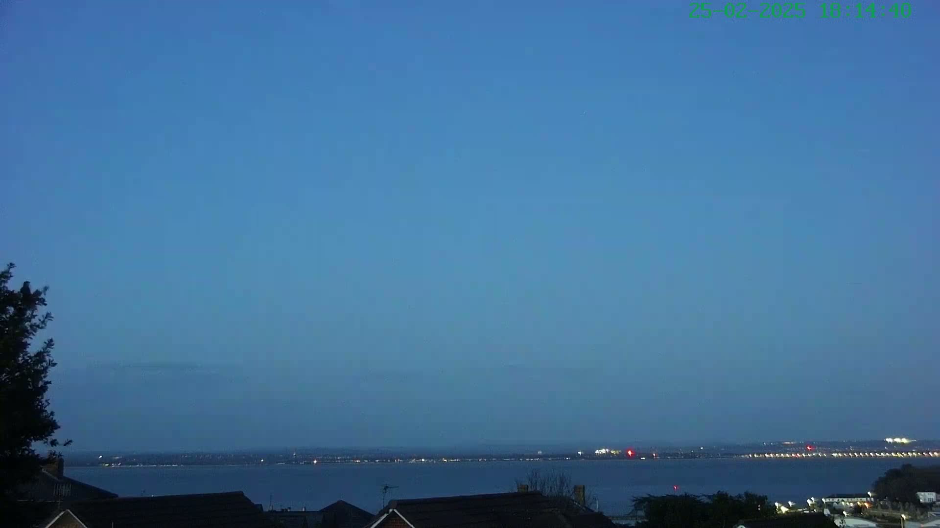 A calm, twilight view shows a body of water with a distant city skyline under a clear, blue sky.