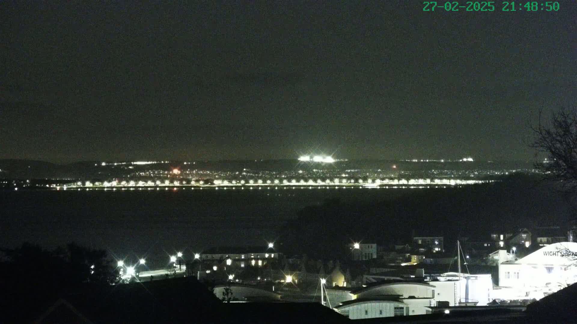 A nighttime view of a city across a body of water, with the city lights clearly visible under a dark, clear sky.