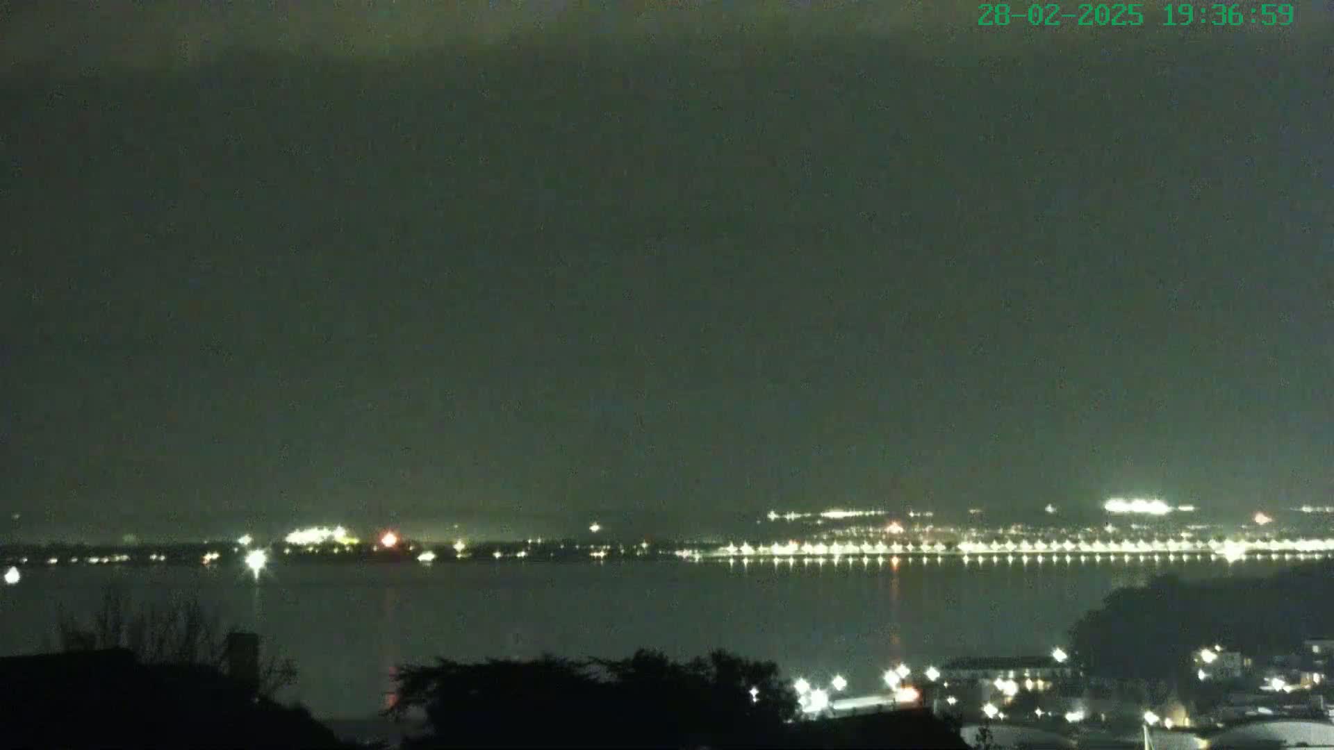 A nighttime view of a city skyline across a body of water under a dark, cloudy sky.