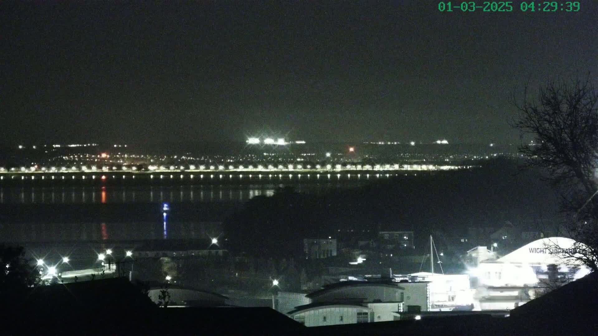 A nighttime view of a city across a body of water, illuminated by lights, under a dark, clear sky.