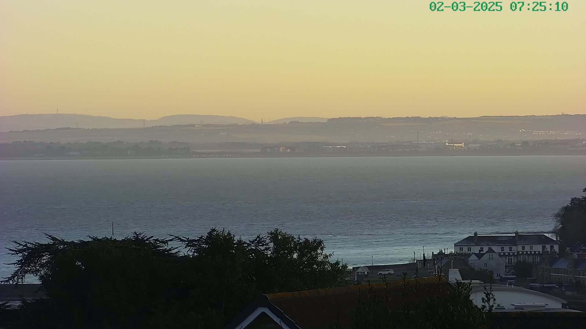 A calm body of water stretches toward distant, hazy hills under a pale yellow-orange sky.