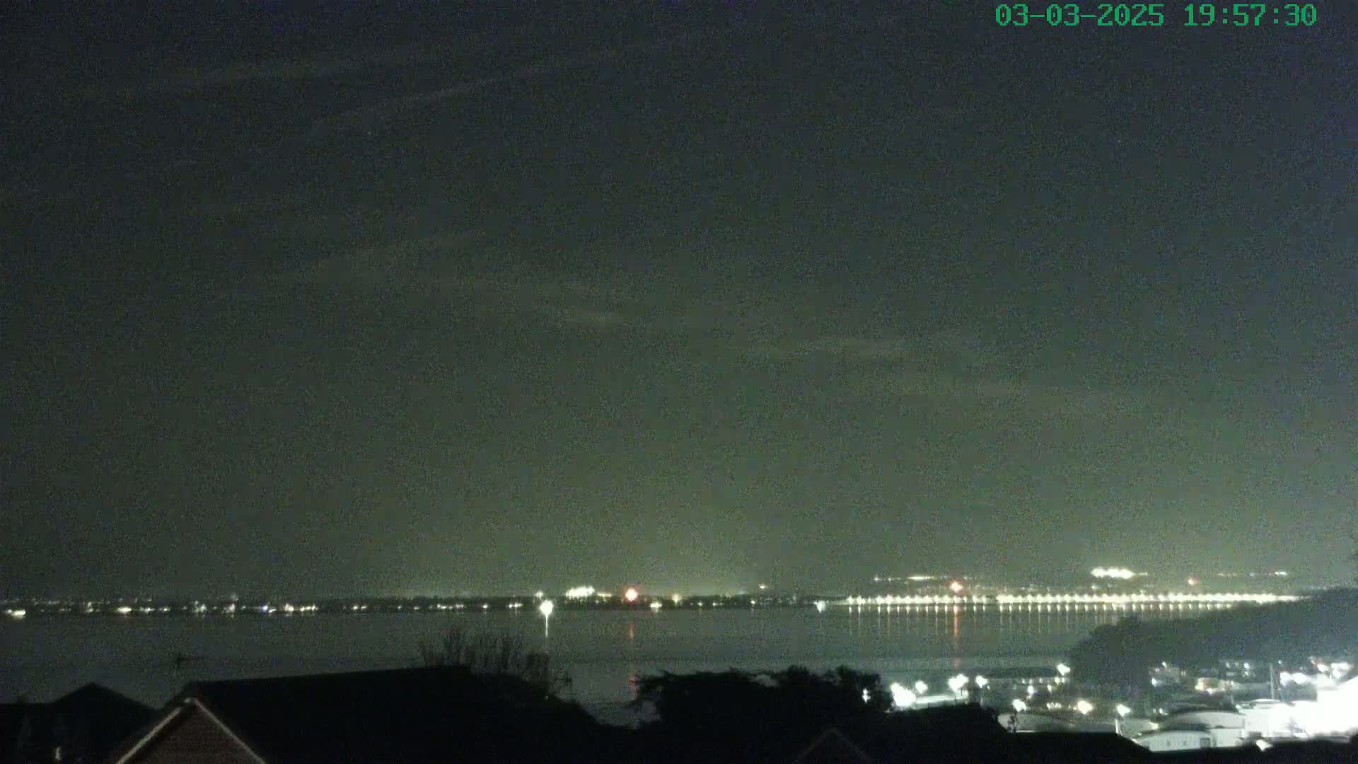 A nighttime view of a body of water with city lights on the far shore under a dark, cloudy sky.