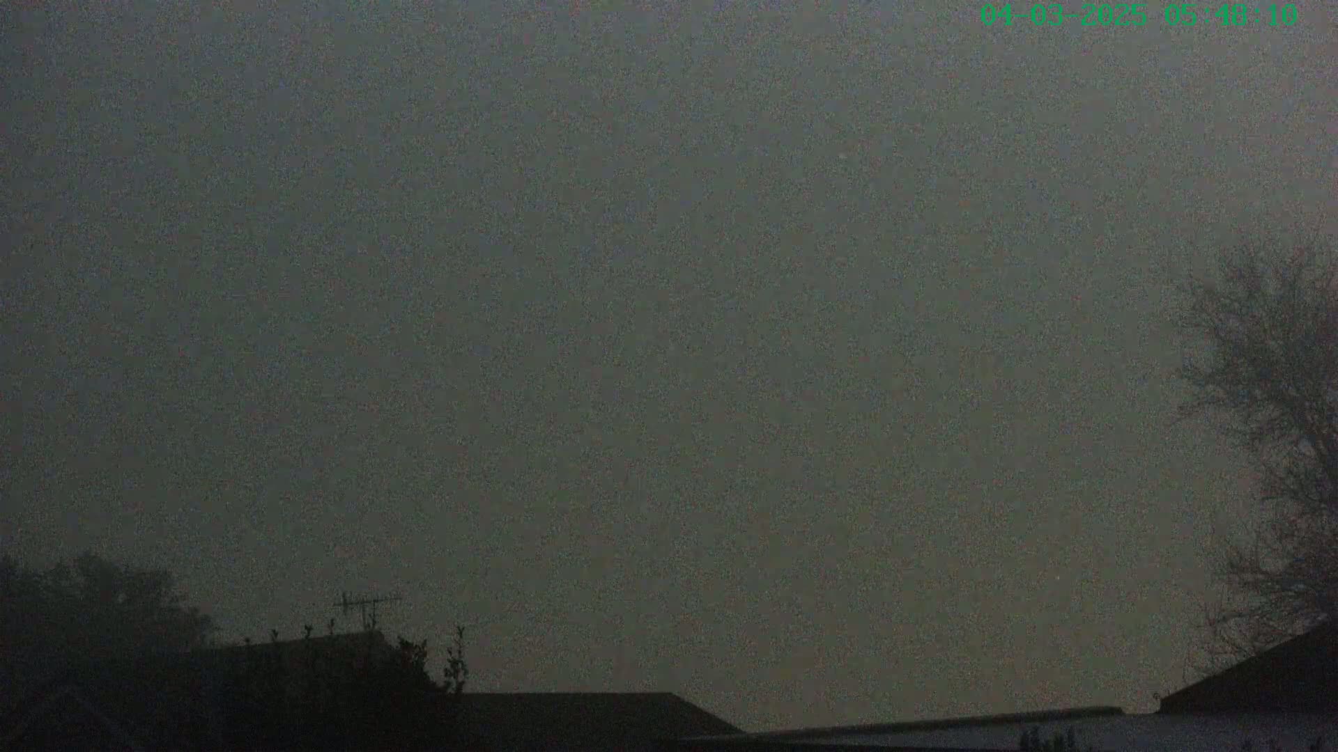 A foggy or hazy sky hangs over a dark silhouette of rooftops and trees.