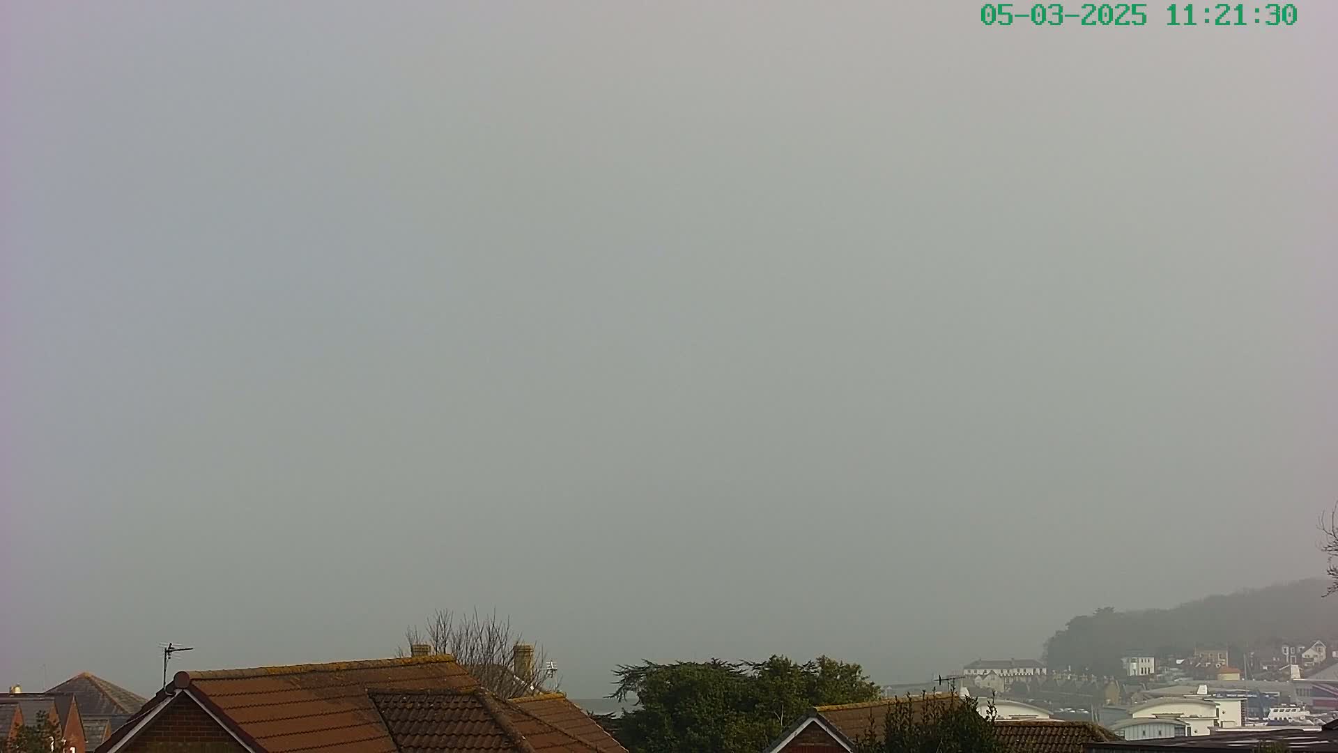 A hazy, foggy view shows the tops of houses with brown tiled roofs and a distant hillside partially obscured by fog.