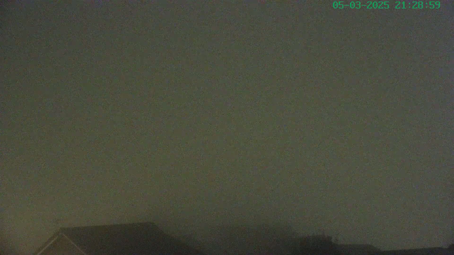A nighttime view shows a foggy sky over the tops of houses.