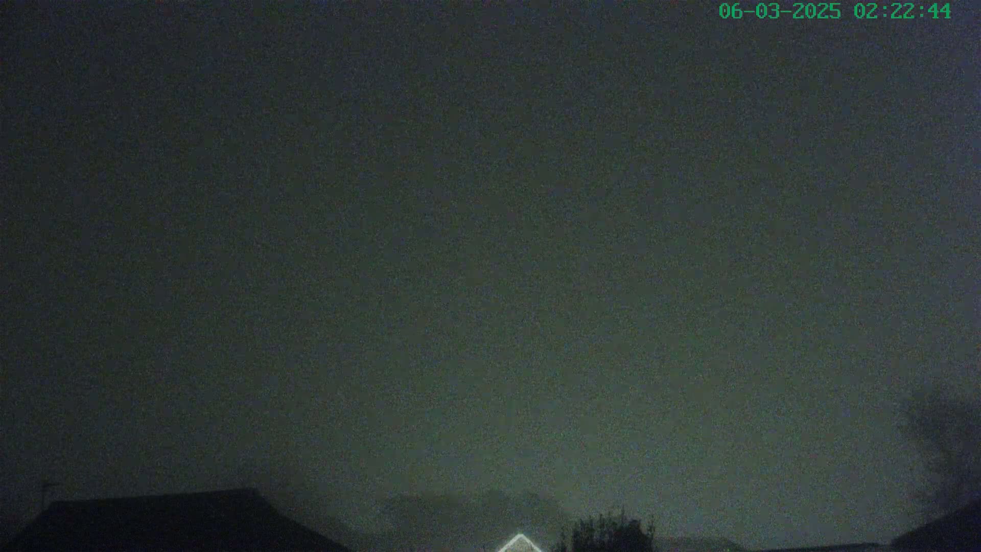 A dark, overcast night sky is visible above the silhouettes of housetops and some trees.