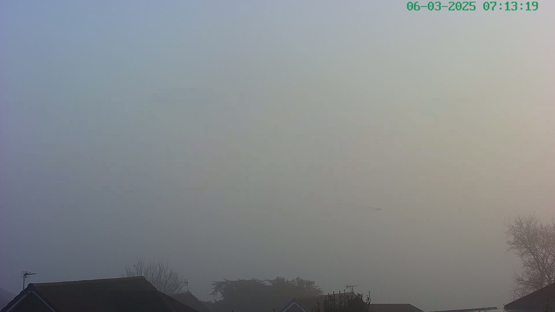 A foggy scene shows the tops of houses and a few trees barely visible in the hazy distance.