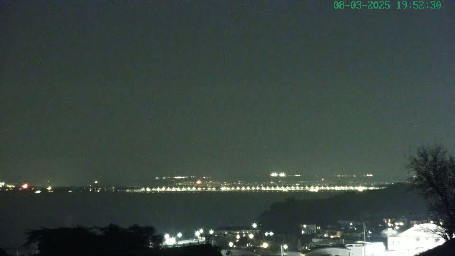 A nighttime view across a body of water shows a distant city skyline illuminated with lights under a dark, clear sky.