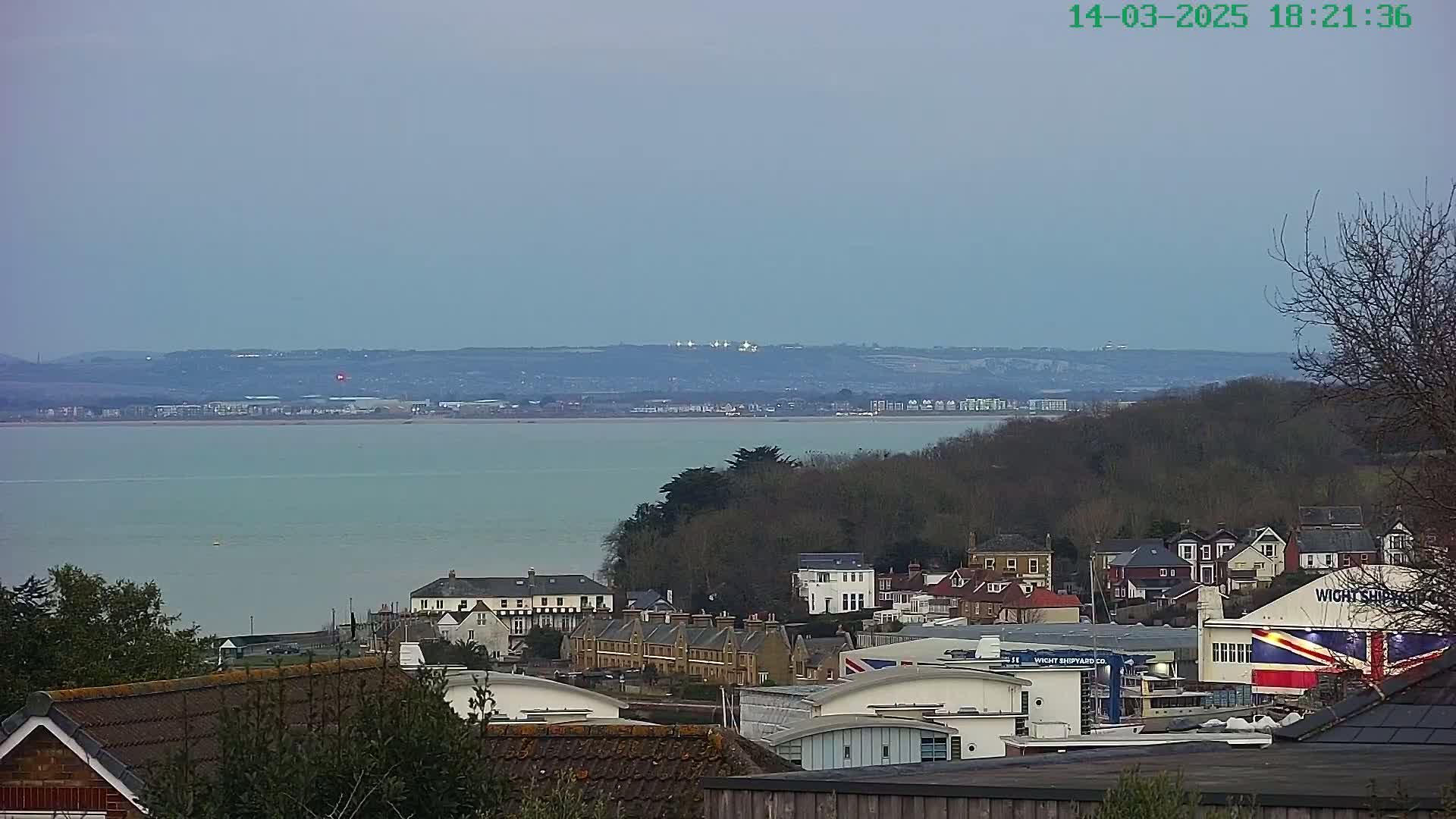 A calm body of water stretches out before a hillside town under a dusky sky.