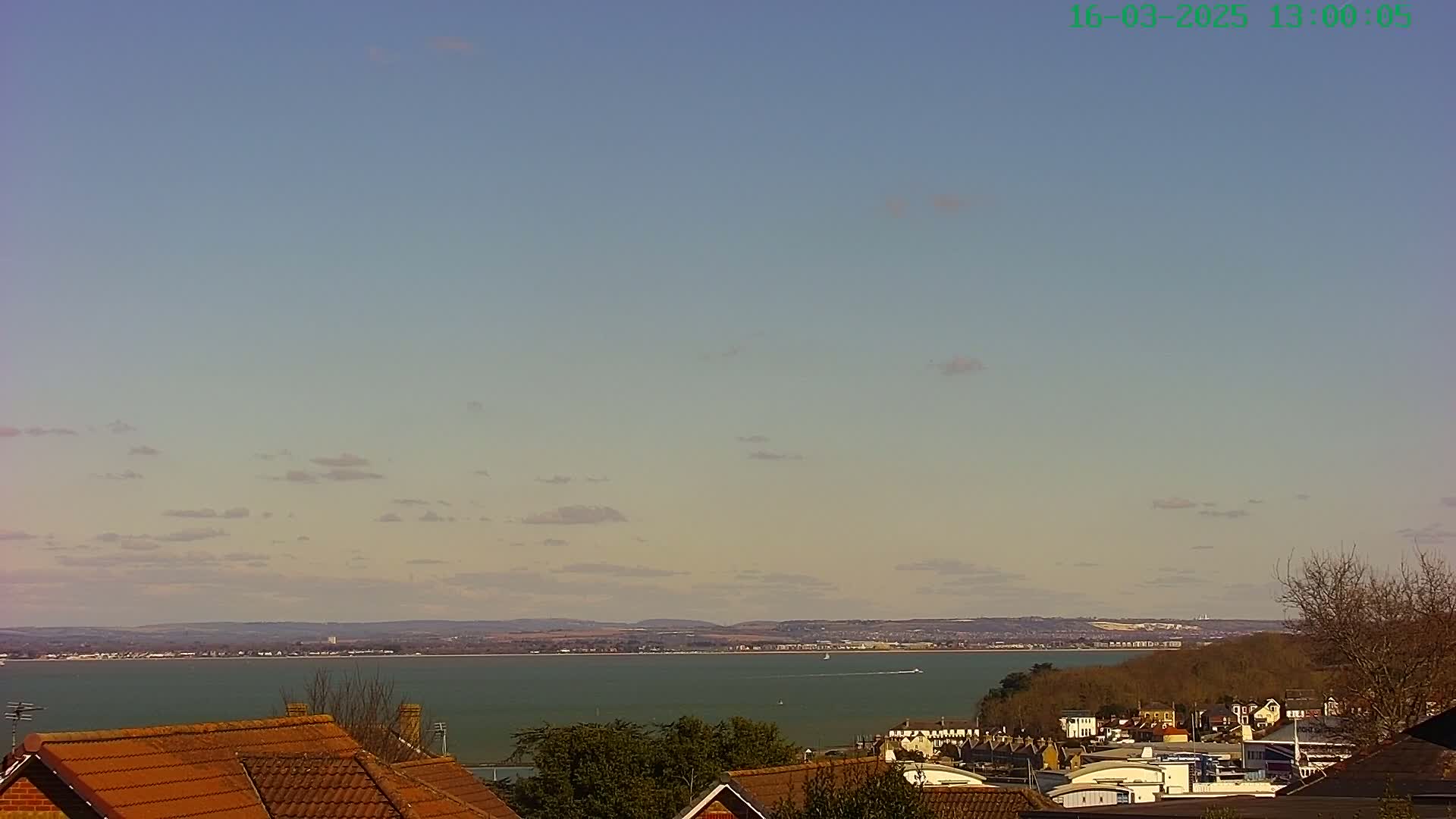 A mostly clear sky overlooks a calm body of water, with distant land and rooftops in the foreground.