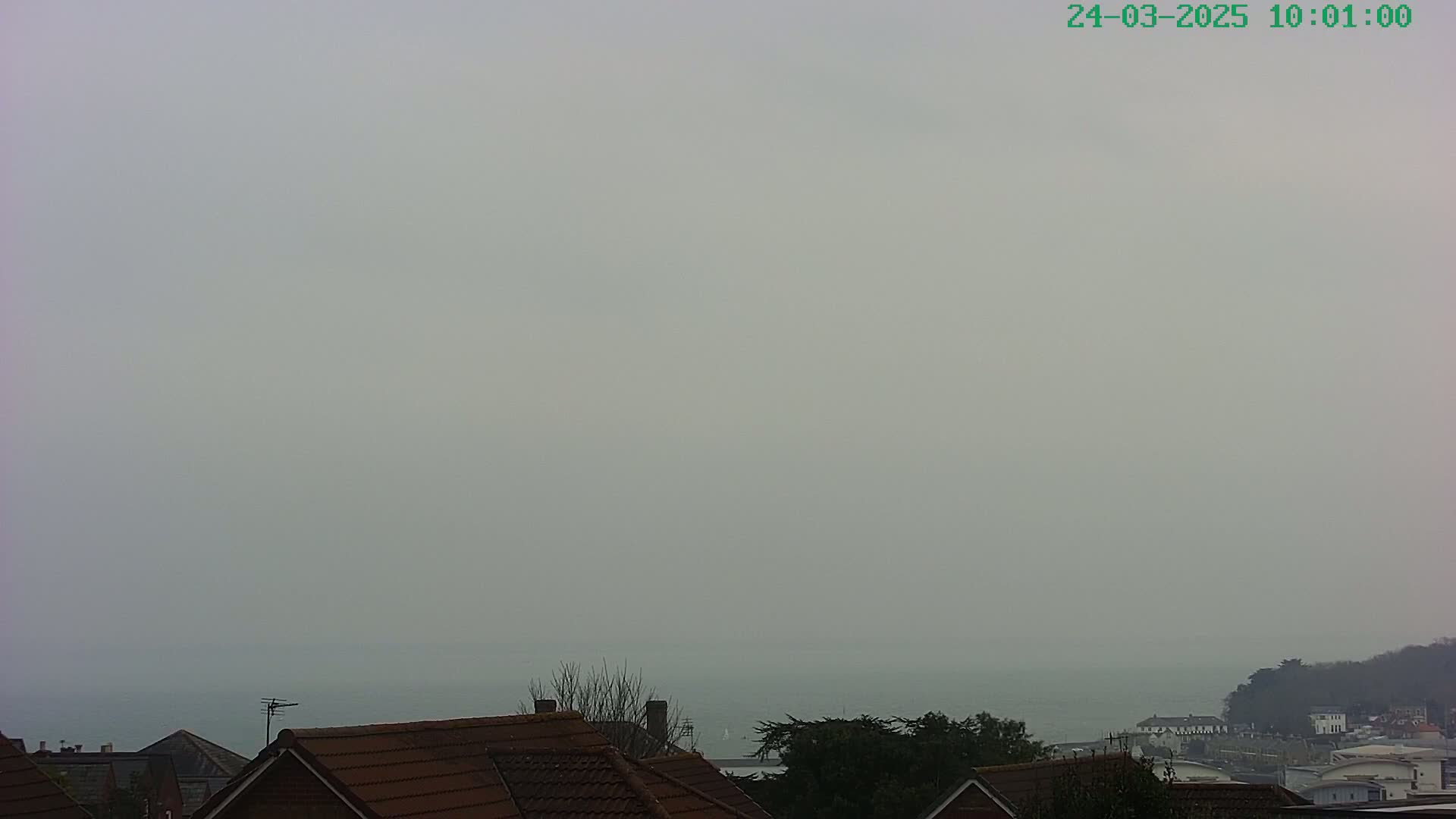 A hazy, overcast view shows a distant body of water behind the brown tiled roofs of houses.