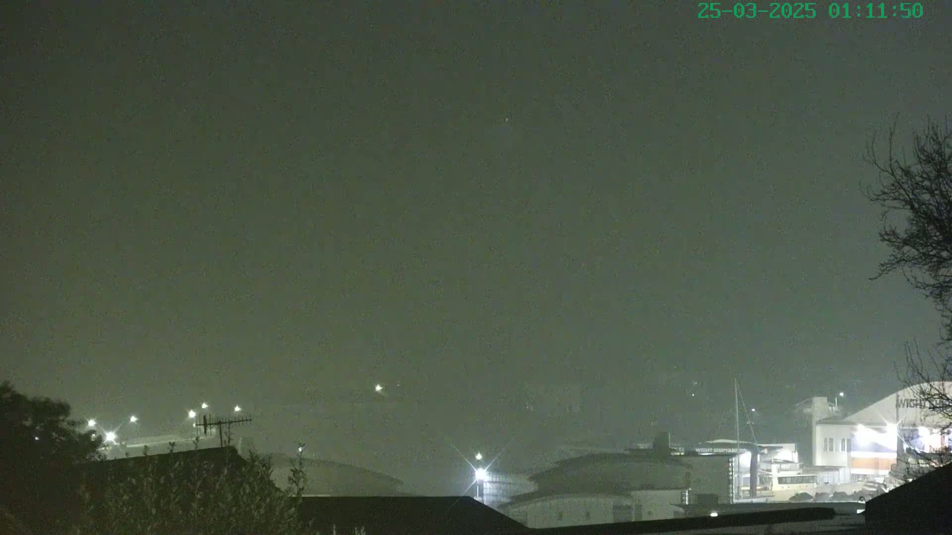 A hazy, nighttime view shows dimly lit buildings and trees under a dark, overcast sky.