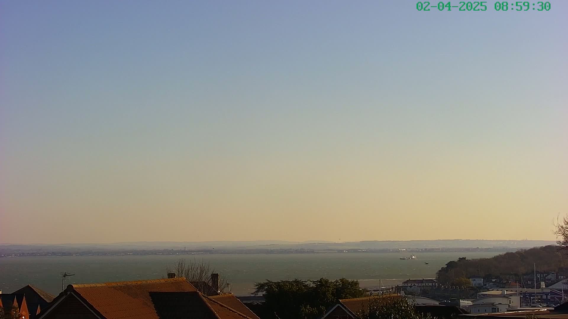 A calm, hazy body of water stretches to a distant shoreline, viewed from a vantage point above rooftops.