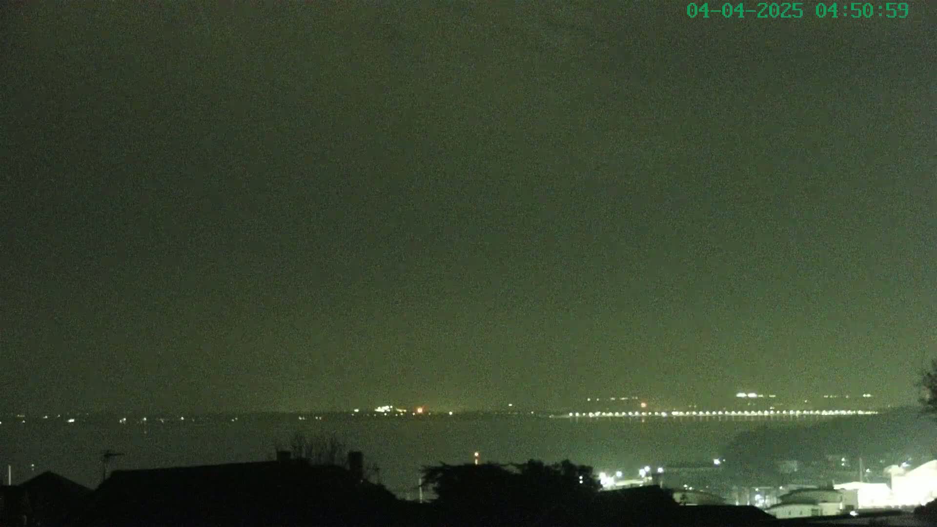 A nighttime view of a body of water with faintly visible lights on the far shore under a dark, hazy sky.