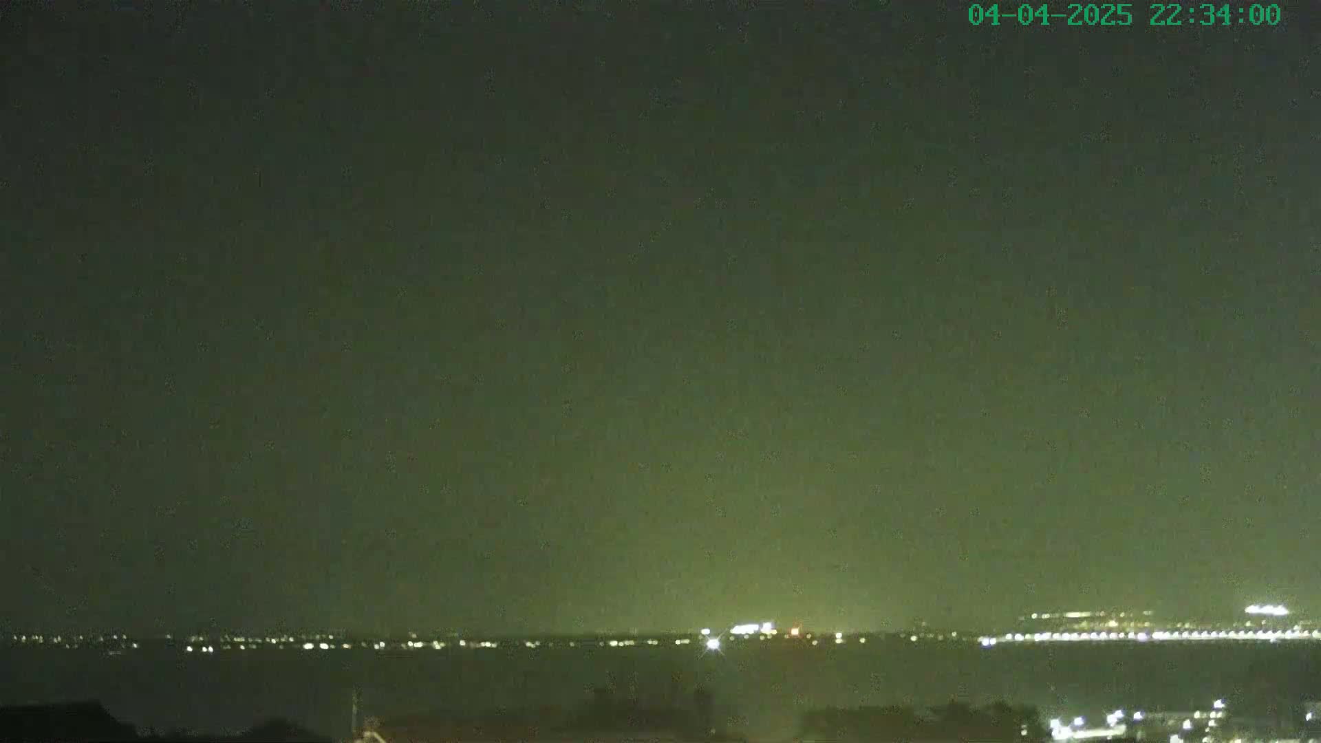 A nighttime view of a body of water with distant city lights visible on the horizon under a dark, possibly cloudy sky.