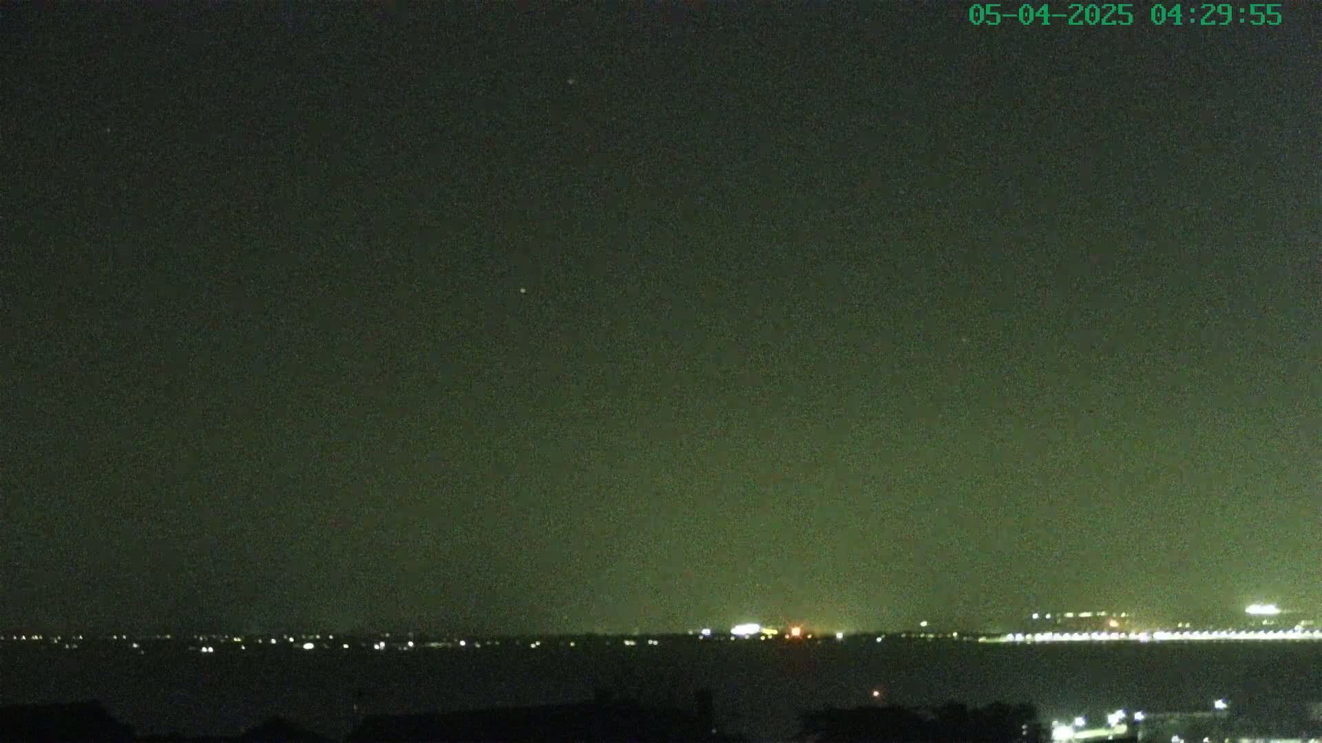 A nighttime view of a body of water with a distant city skyline faintly illuminated under a dark, possibly hazy, sky.