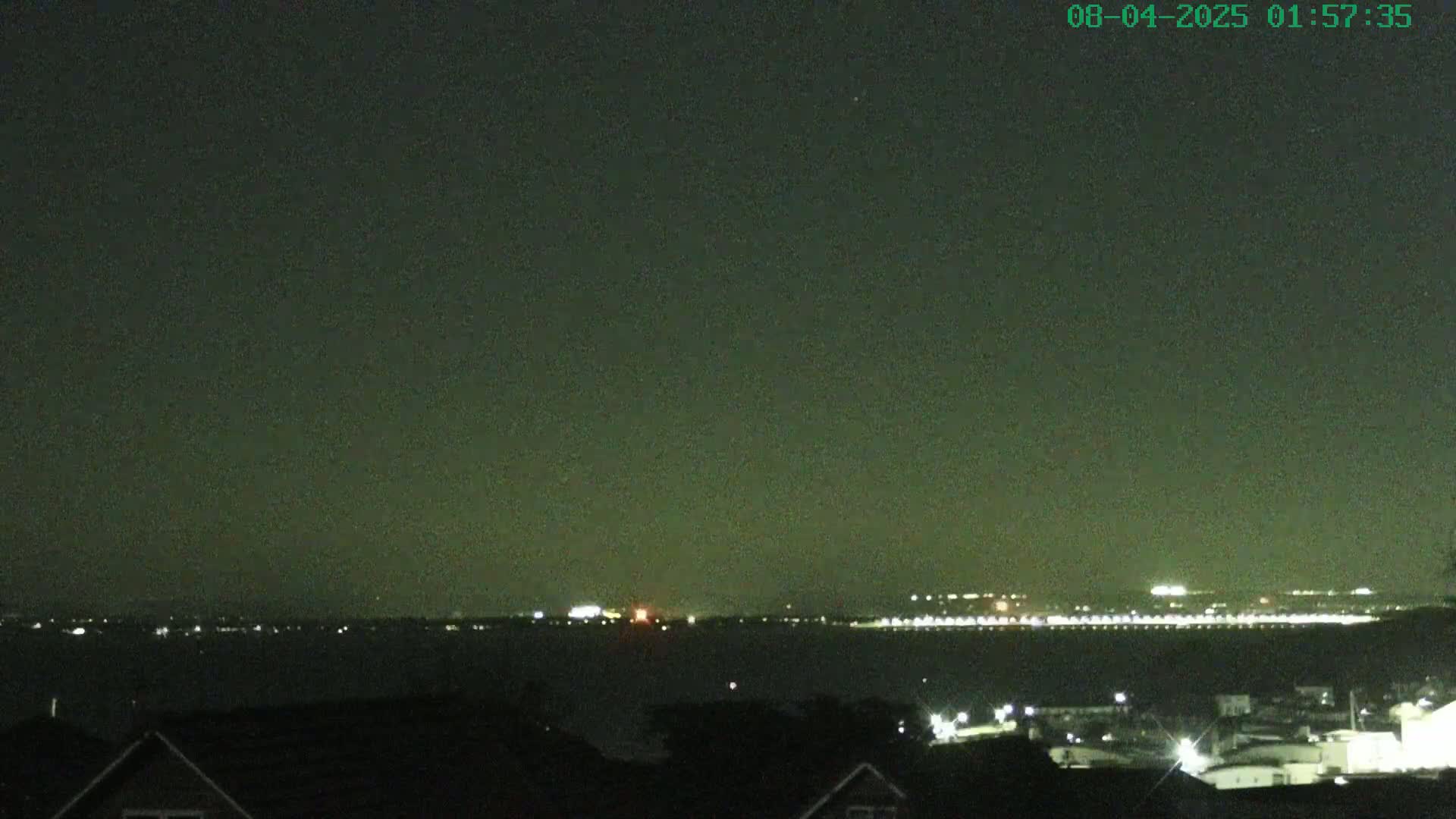 A nighttime view shows a body of water with distant city lights under a dark, clear sky.