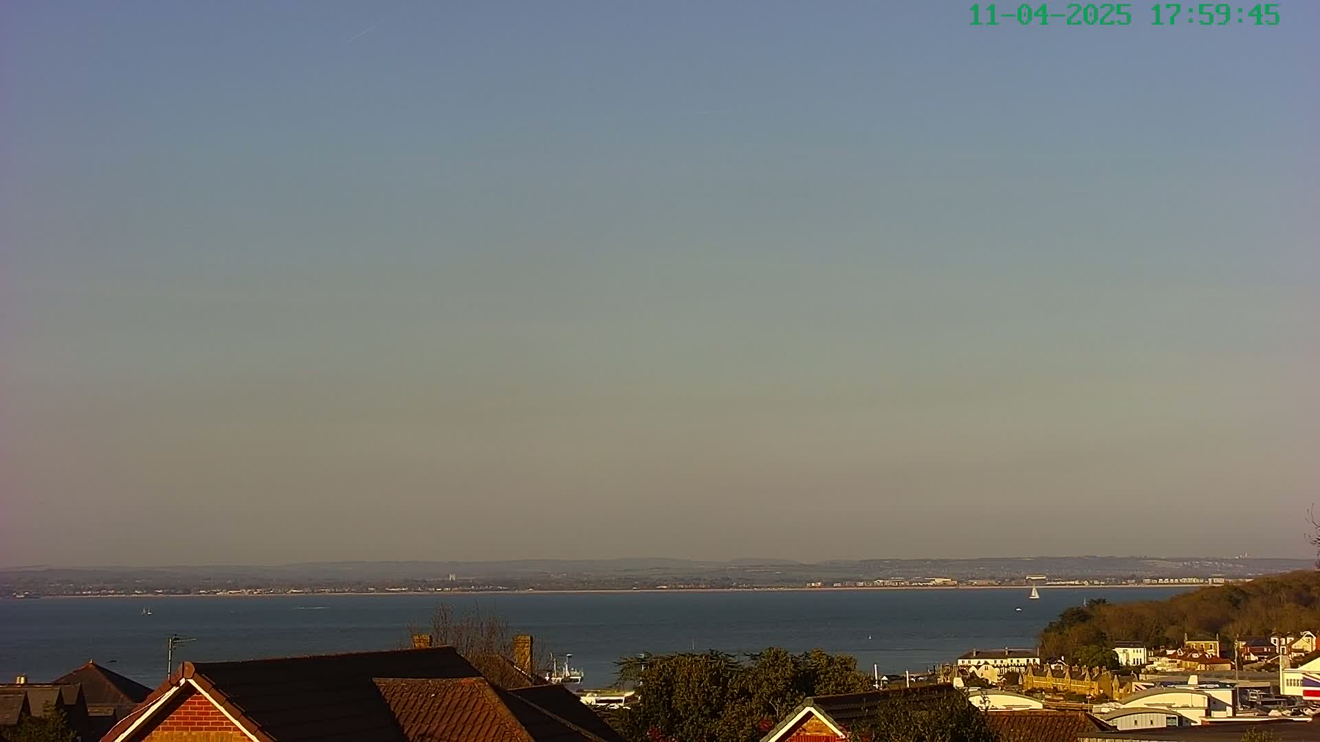 A calm body of water is visible beyond a line of houses, under a clear, pale sky.