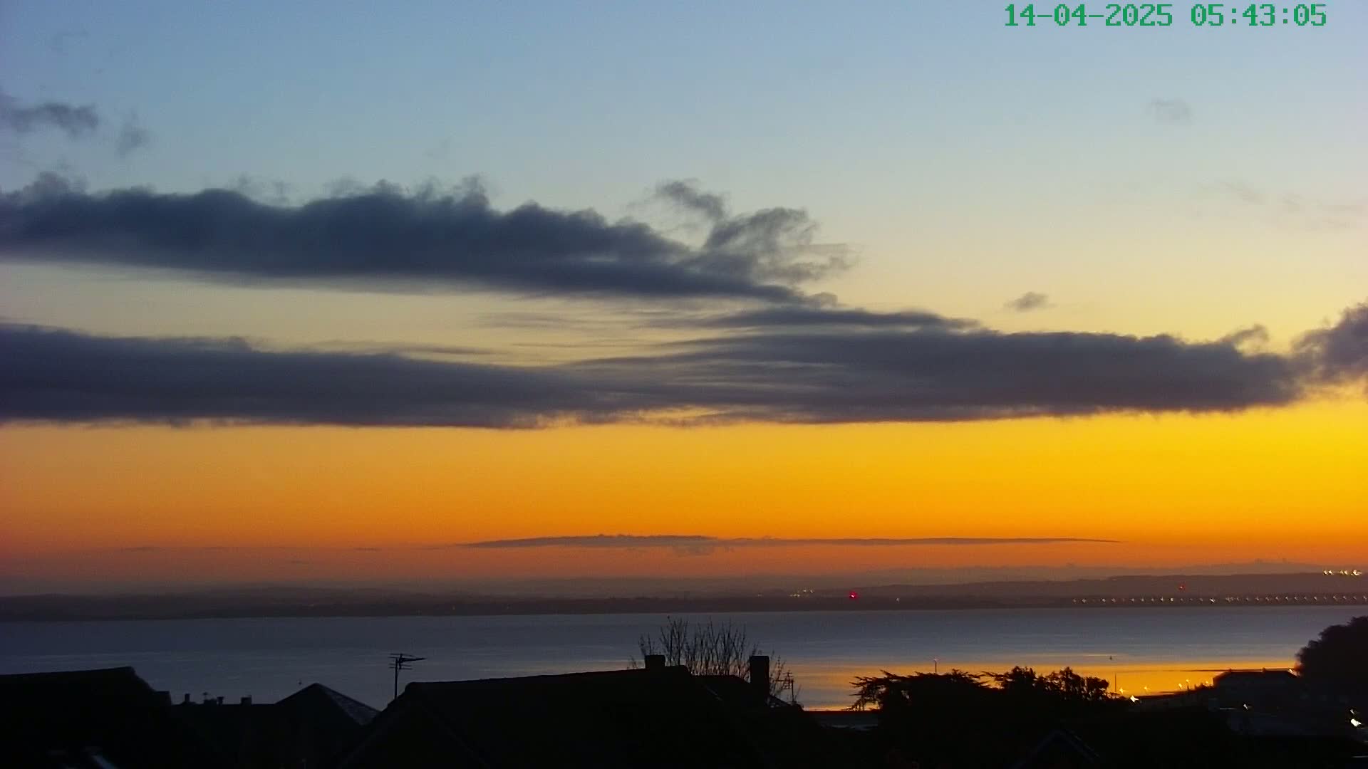 A sunrise over a calm body of water, with dark clouds layered across a vibrant orange and yellow sky.