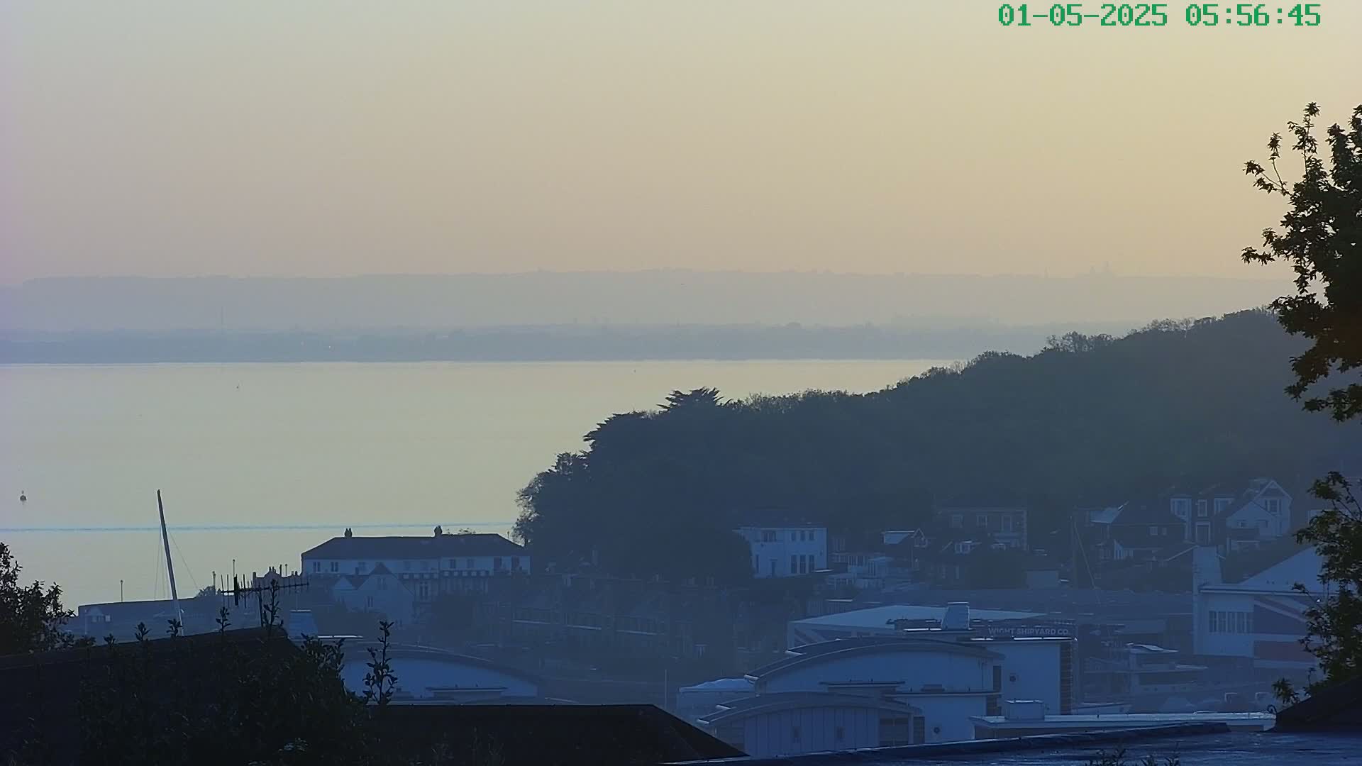 A hazy, dawn-lit view of a calm body of water, with a coastal town nestled amongst hills on the far side.