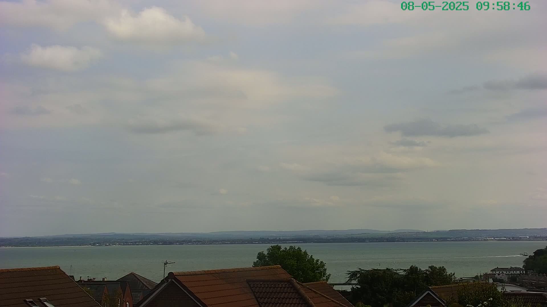 A partly cloudy sky overlooks a calm body of water and the rooftops of houses.