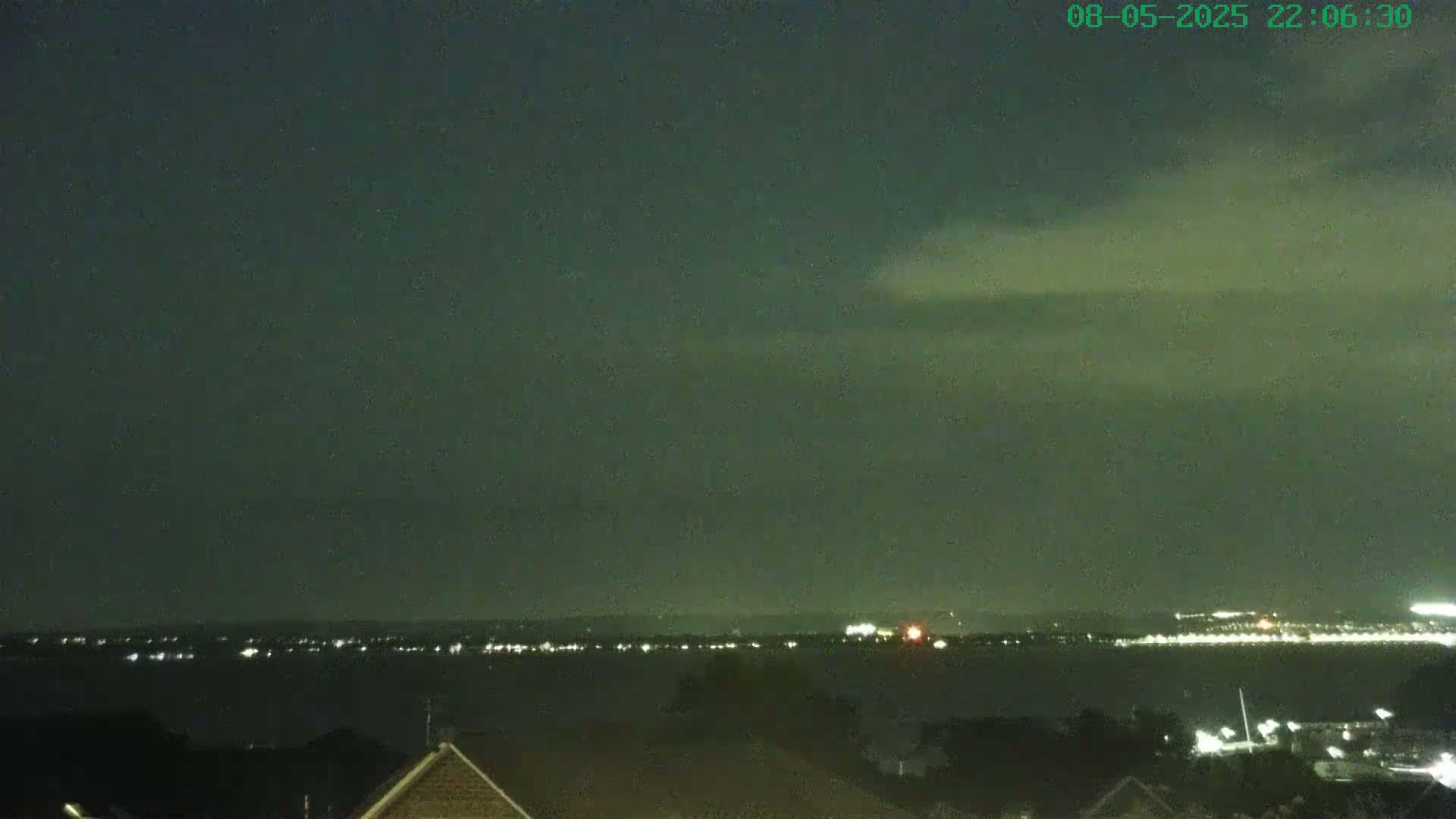 A nighttime view shows a body of water with a distant city skyline faintly illuminated, under a dark, cloudy sky.