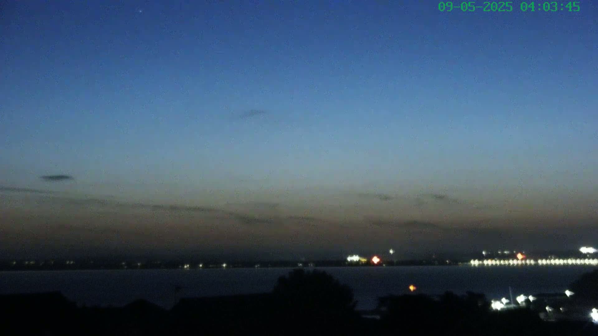 A dark body of water is visible at twilight under a mostly clear, dark blue sky with a few faint clouds.