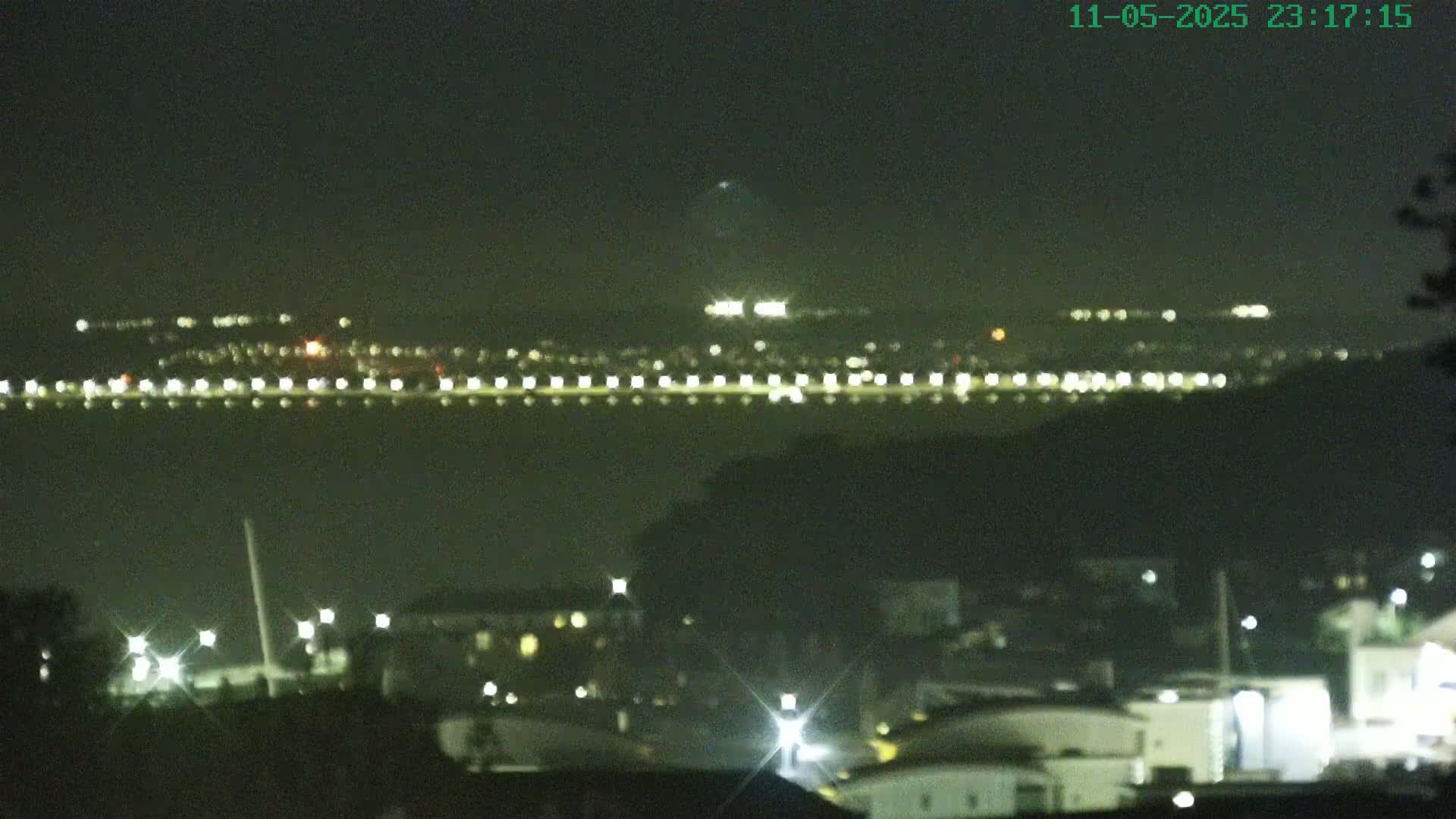 A nighttime view of a city across a body of water, illuminated by numerous lights.