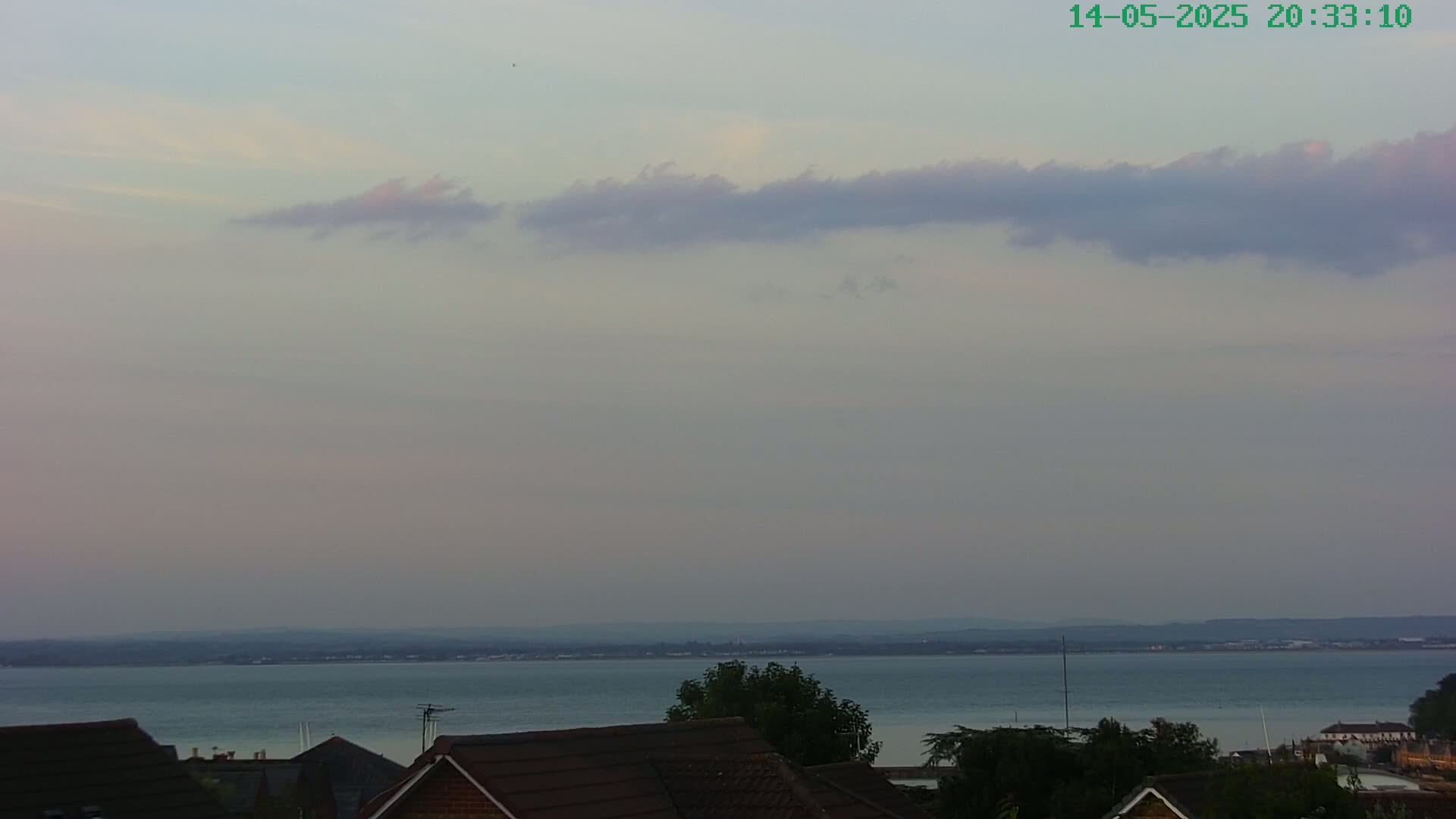 A calm body of water stretches to a distant shoreline under a pale, cloudy twilight sky.